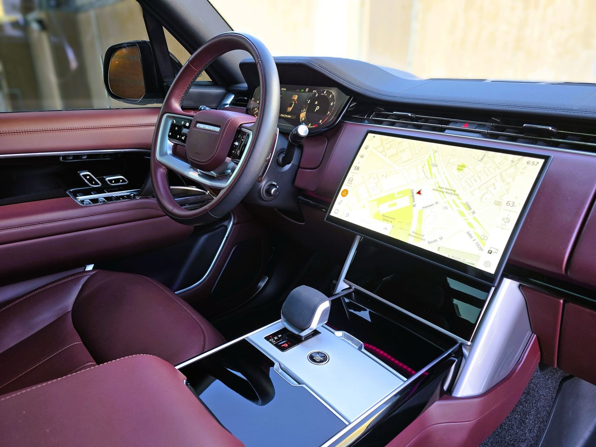 Interior of a red Range Rover with a large touchscreen display and burgundy leather seats.