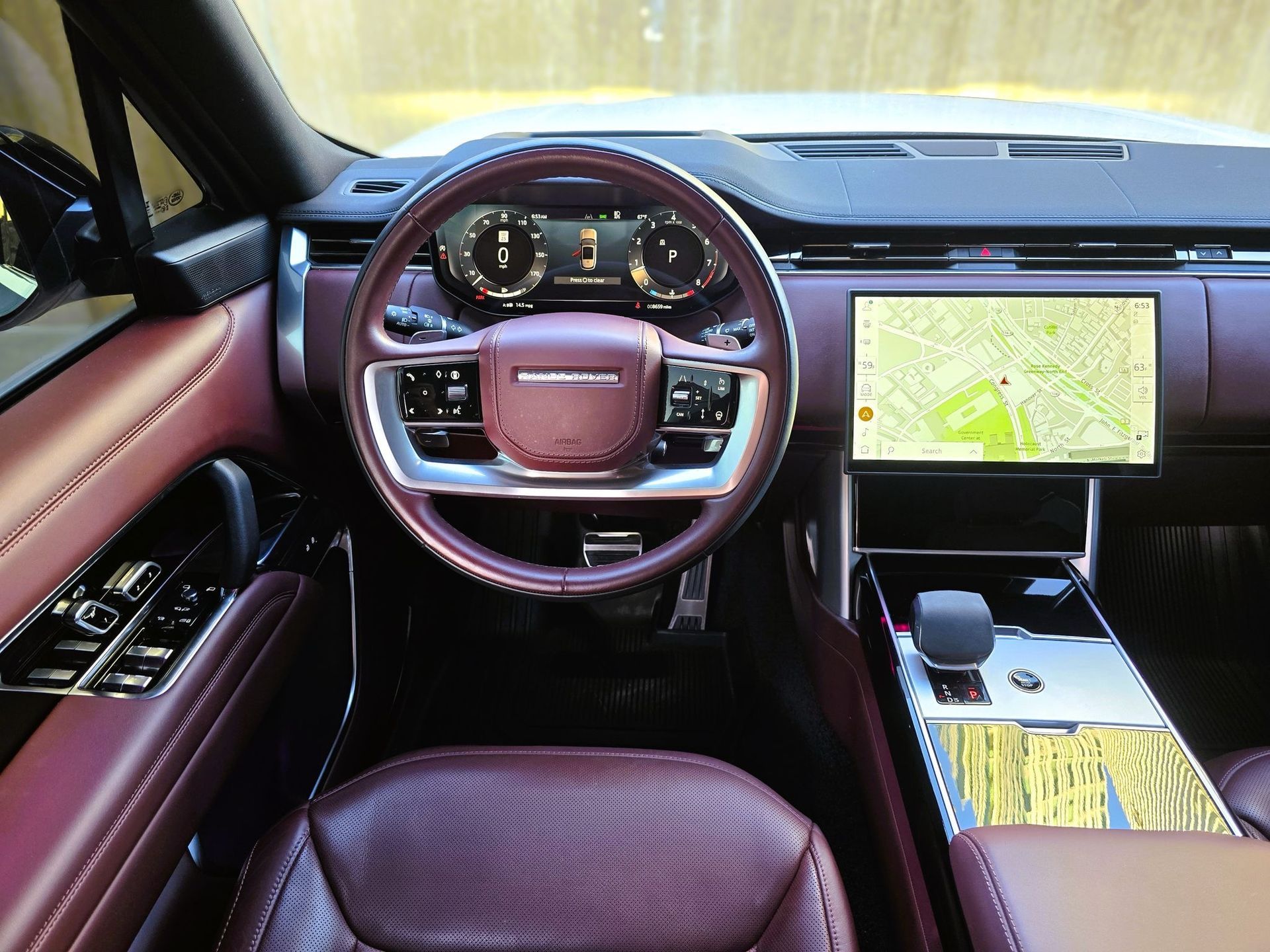 Interior of a luxury SUV, dark red leather seats and steering wheel, digital dashboard displaying navigation.