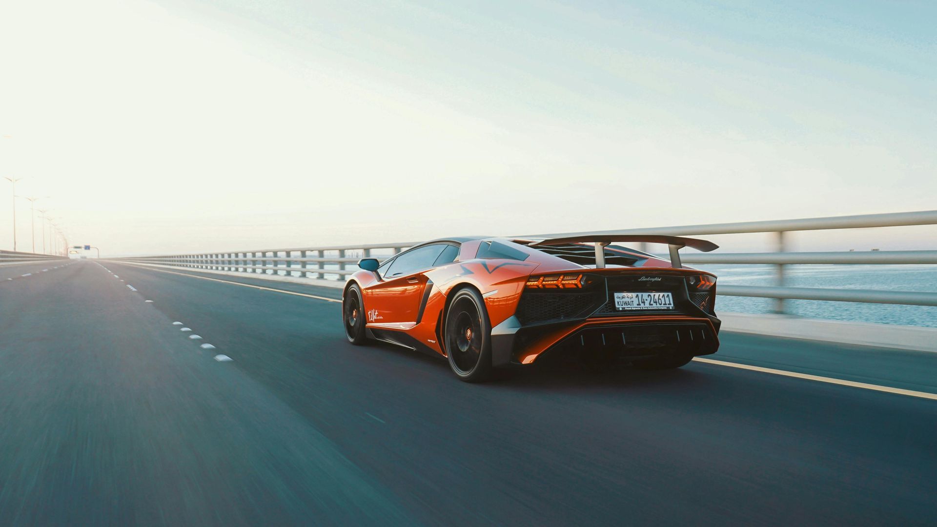 Orange Lamborghini driving fast on a bridge with a clear sky.