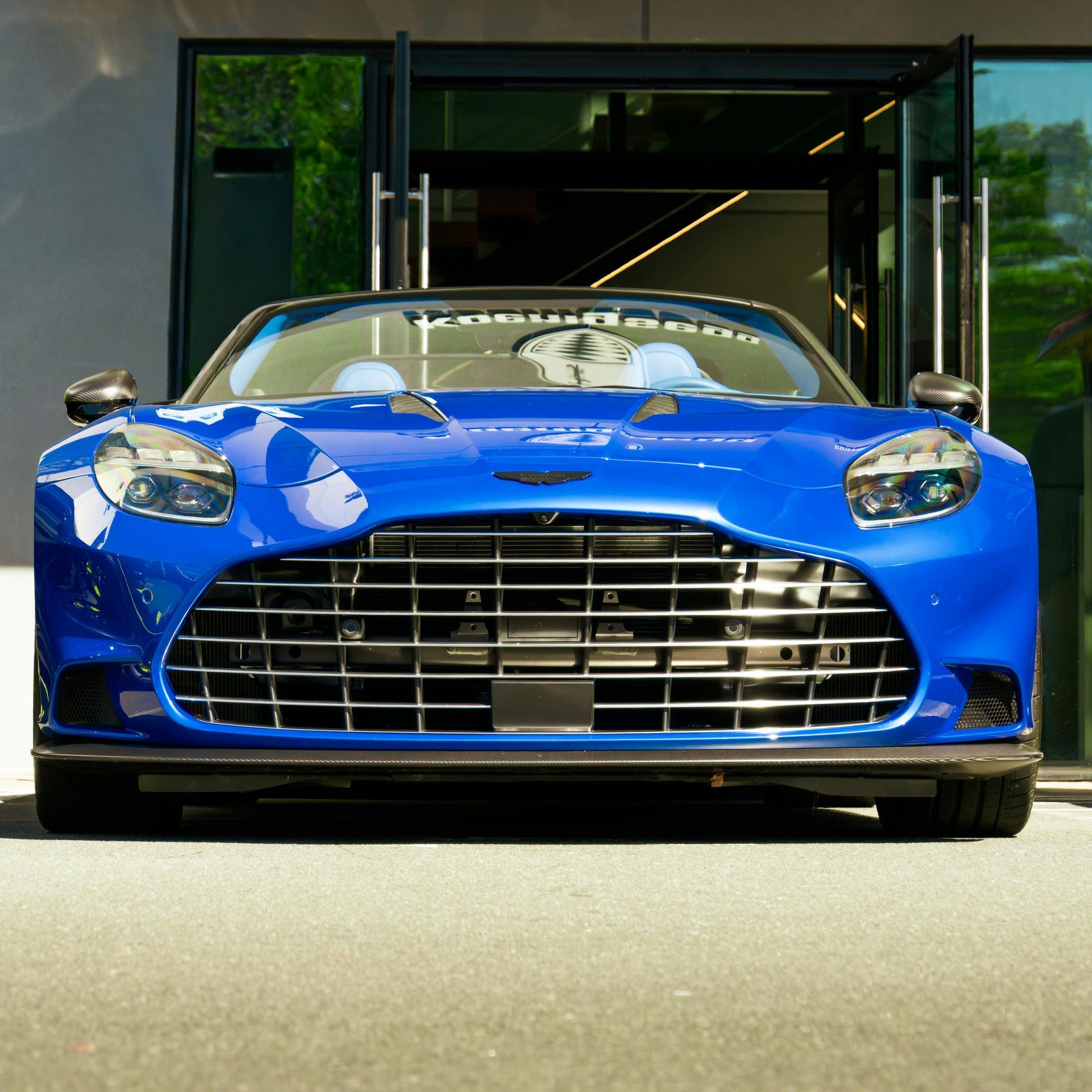 Blue Aston Martin parked in front of a building with open doors.