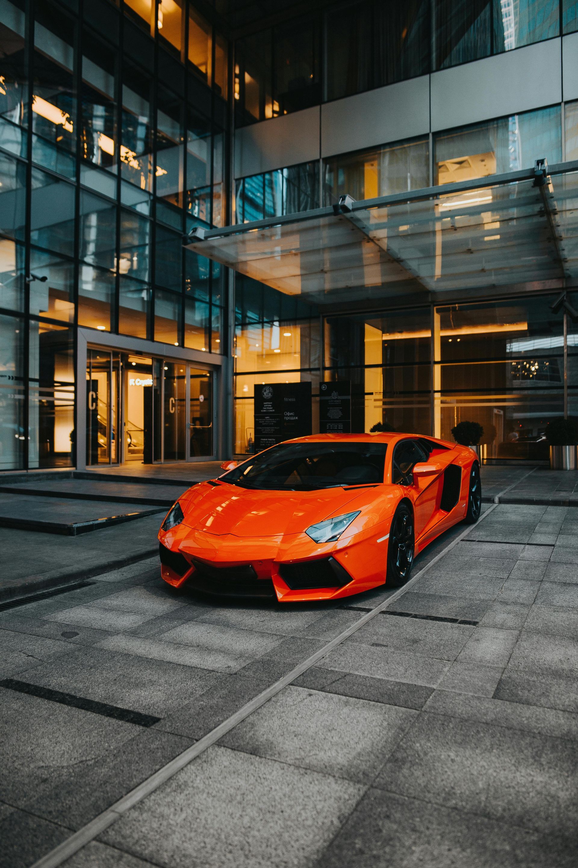 Orange Lamborghini parked in front of a modern building entrance with glass and metallic features.