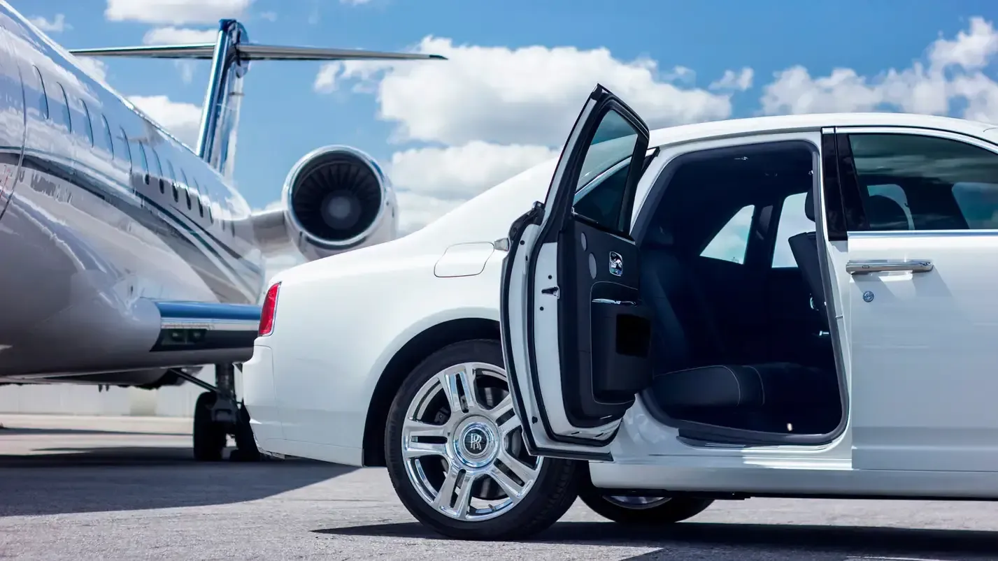 Man in a suit stands in front of a black SUV in a parking lot.