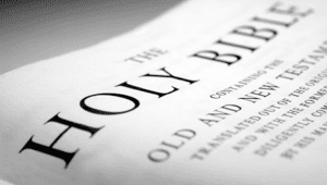 A black and white, angled close-up of a page from the Holy Bible, showing the title and text details.