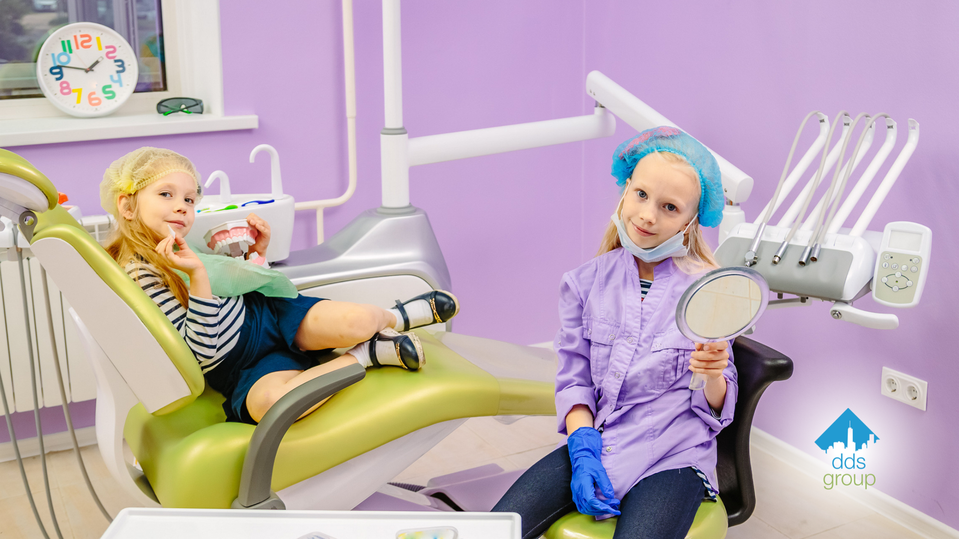 A little girl is sitting in a dental chair and looking at her teeth in a mirror.