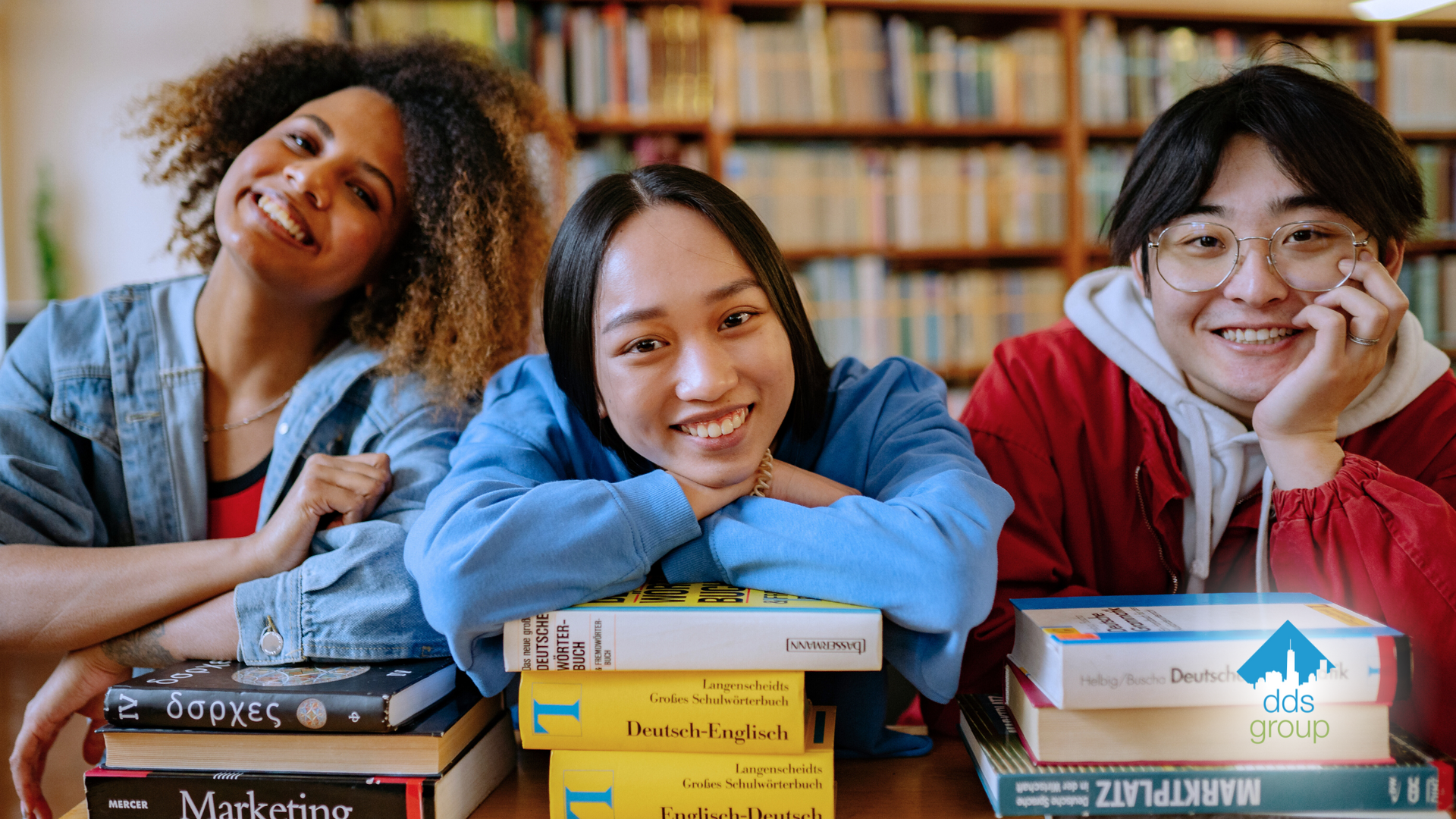 A group of young people are sitting at a table with stacks of books.