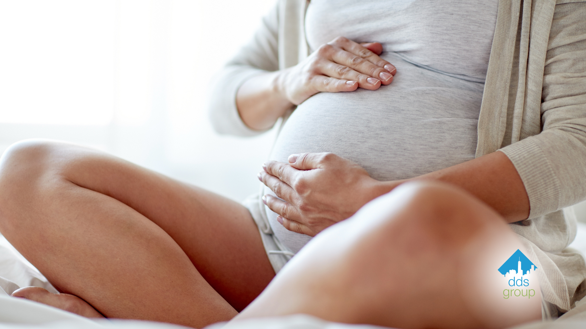 A pregnant woman is sitting on a bed holding her belly.