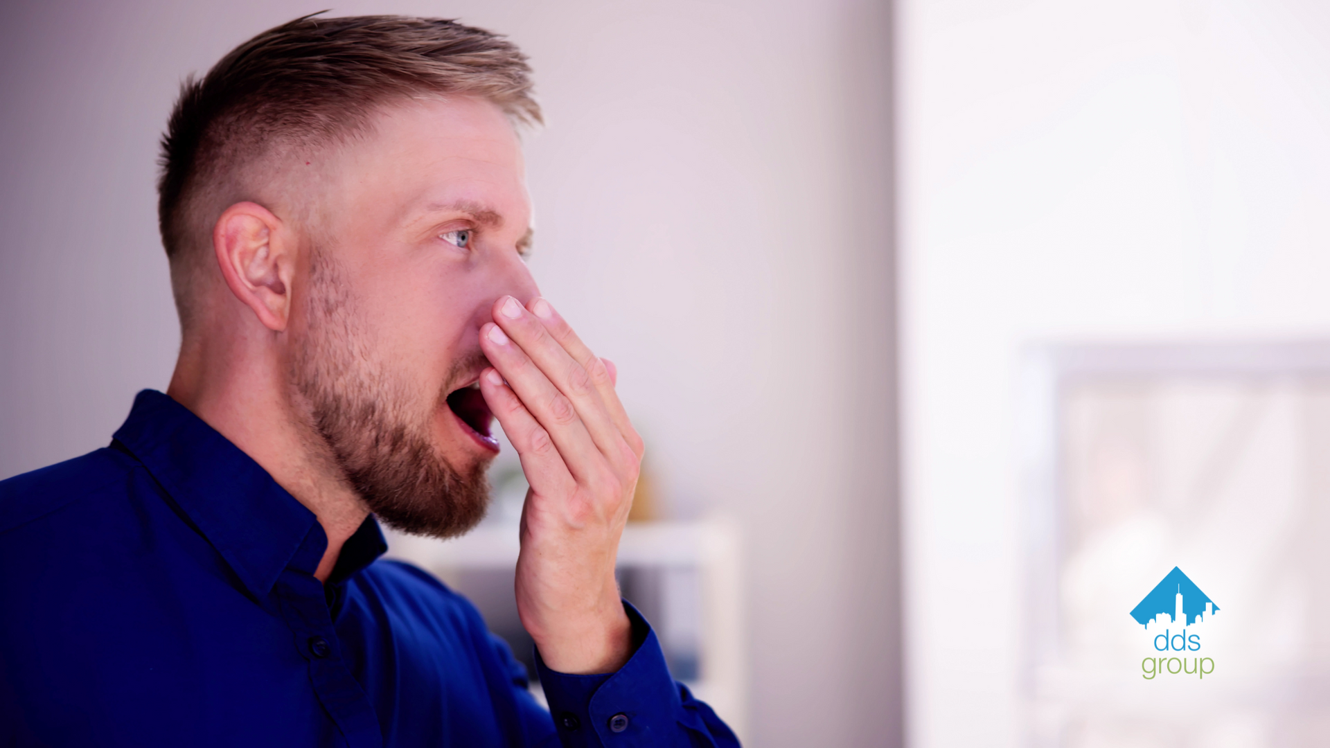 A man in a blue shirt is covering his mouth with his hand.