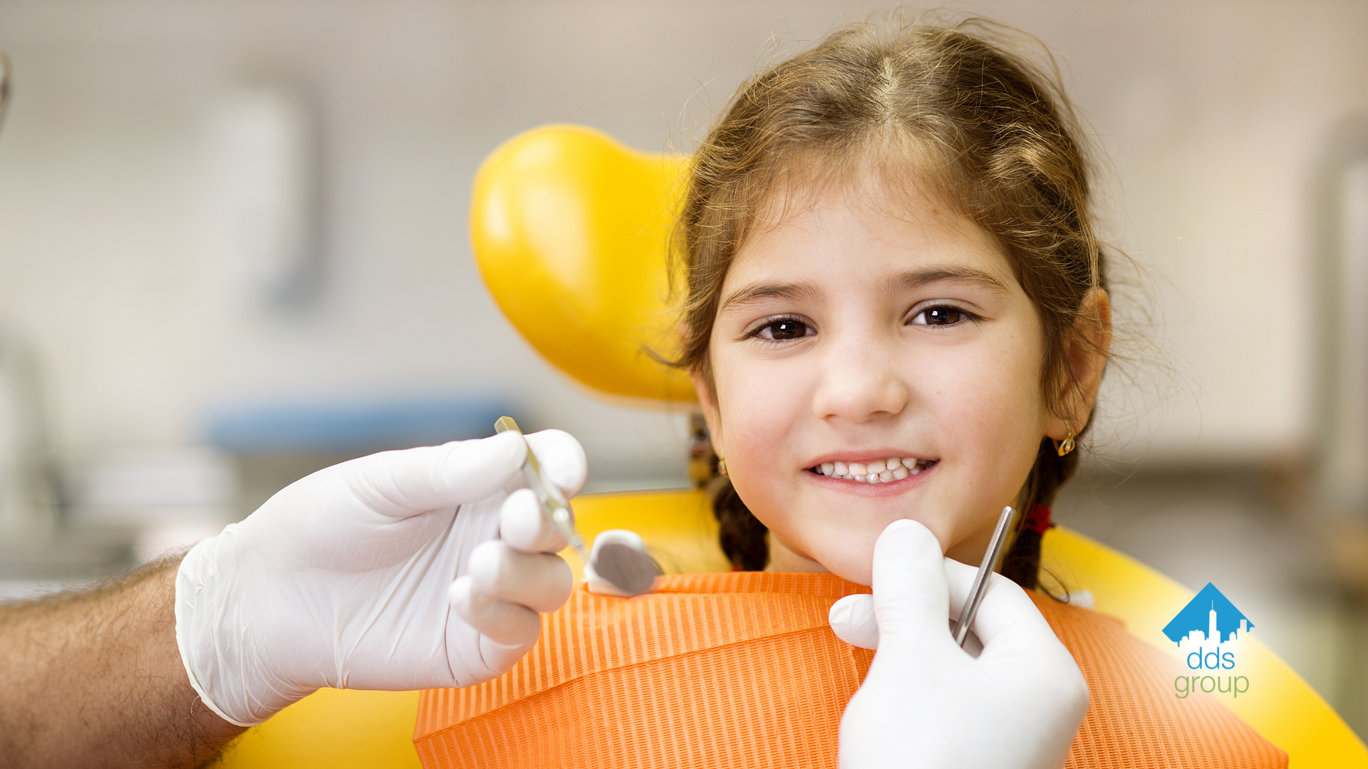 A little girl is sitting in a dental chair while a dentist examines her teeth.