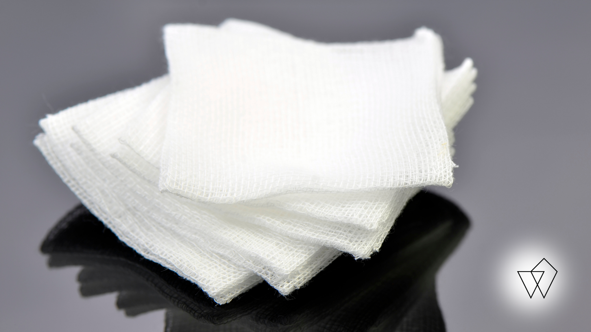 Stack of white, square gauze pads; reflective surface behind them.