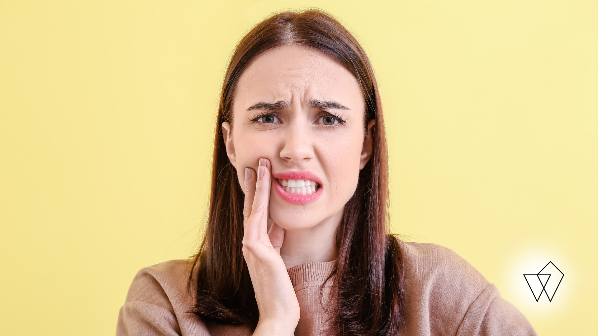 Woman holding cheek, grimacing, with expression of pain; yellow background.