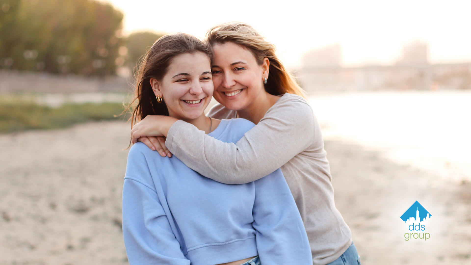 A mother and daughter are hugging each other on the beach.