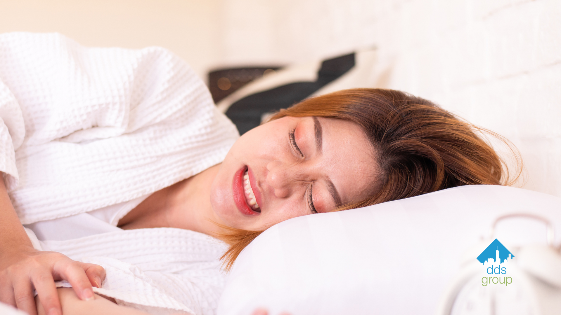 A woman is sleeping on a bed with her eyes closed and smiling.