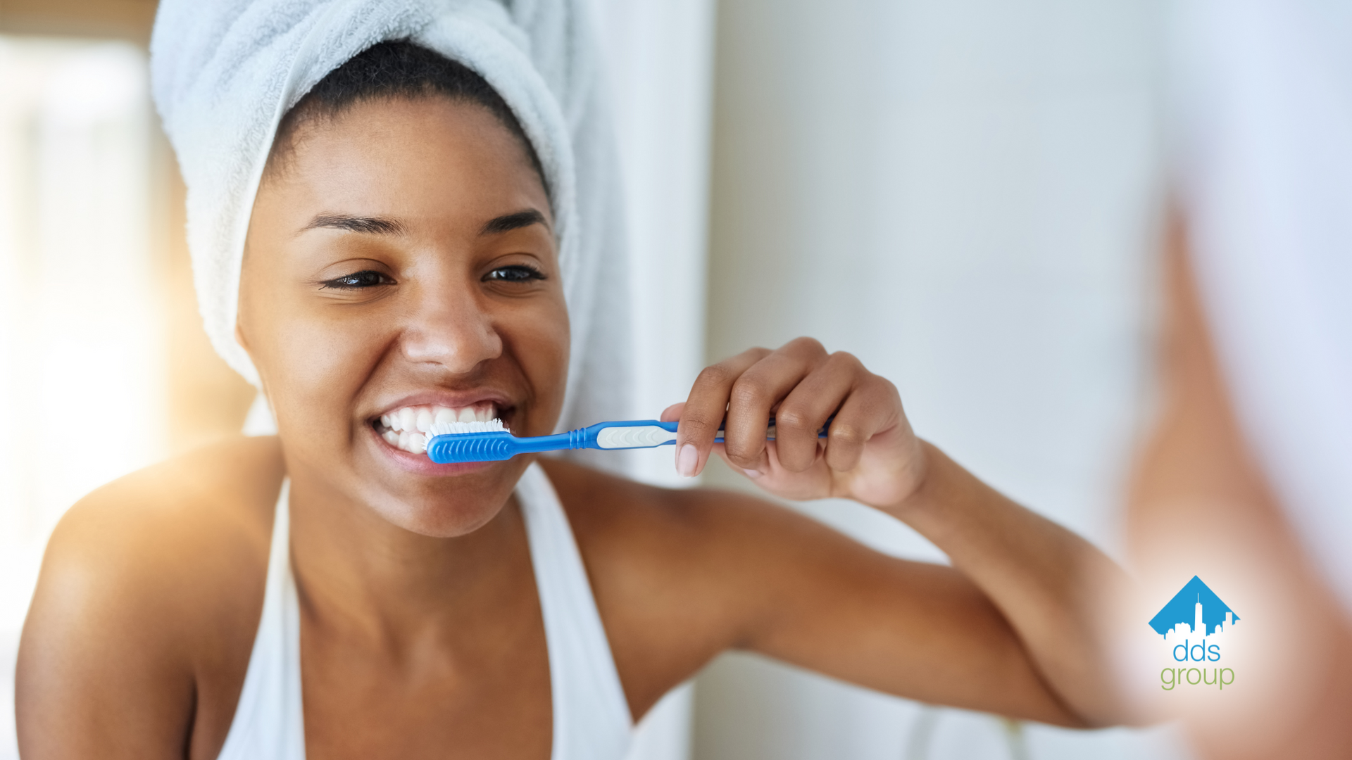 A woman with a towel wrapped around her head is brushing her teeth in front of a mirror.