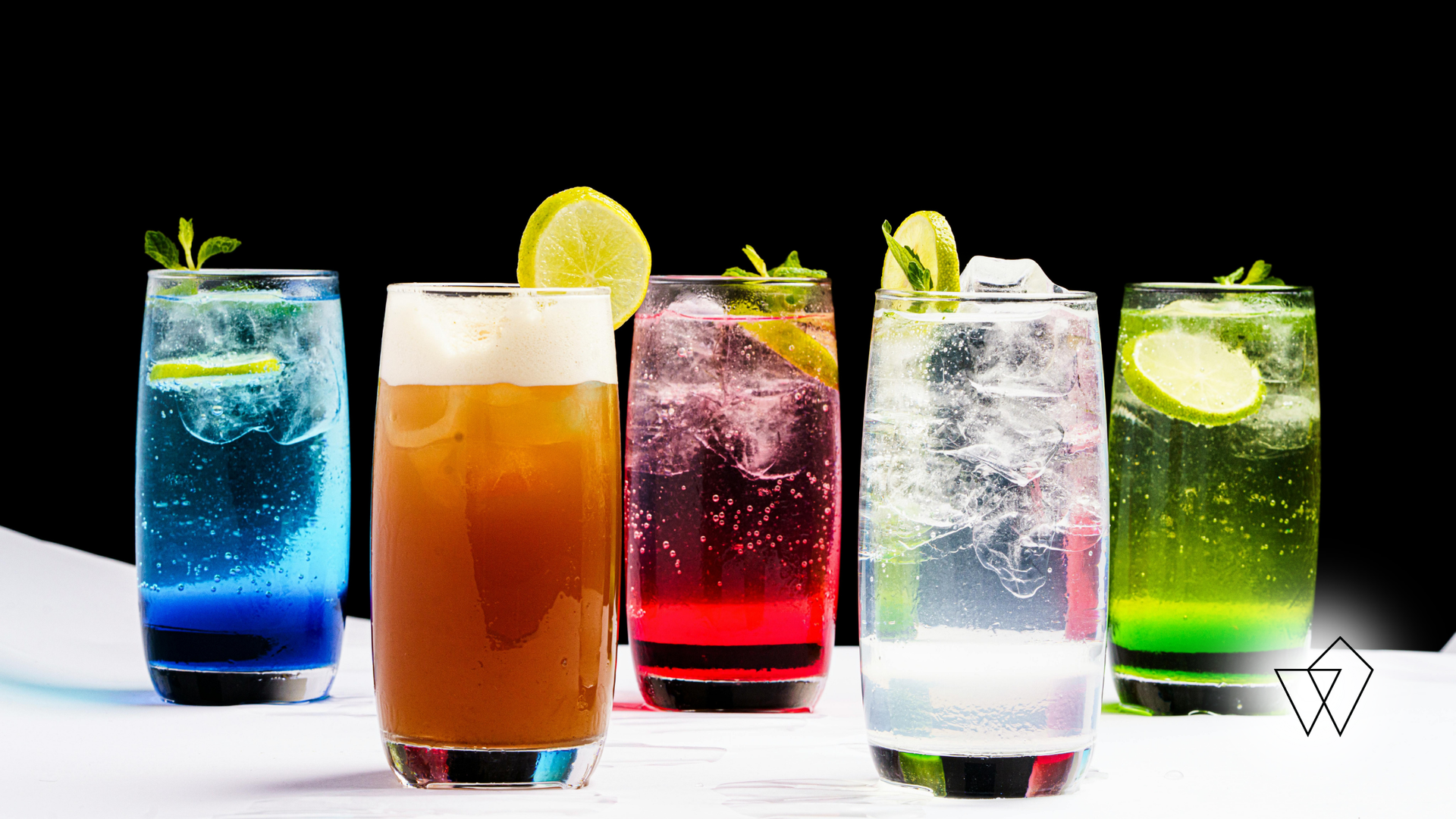 Five colorful cocktails in tall glasses, garnished with lime and mint, against a black backdrop.