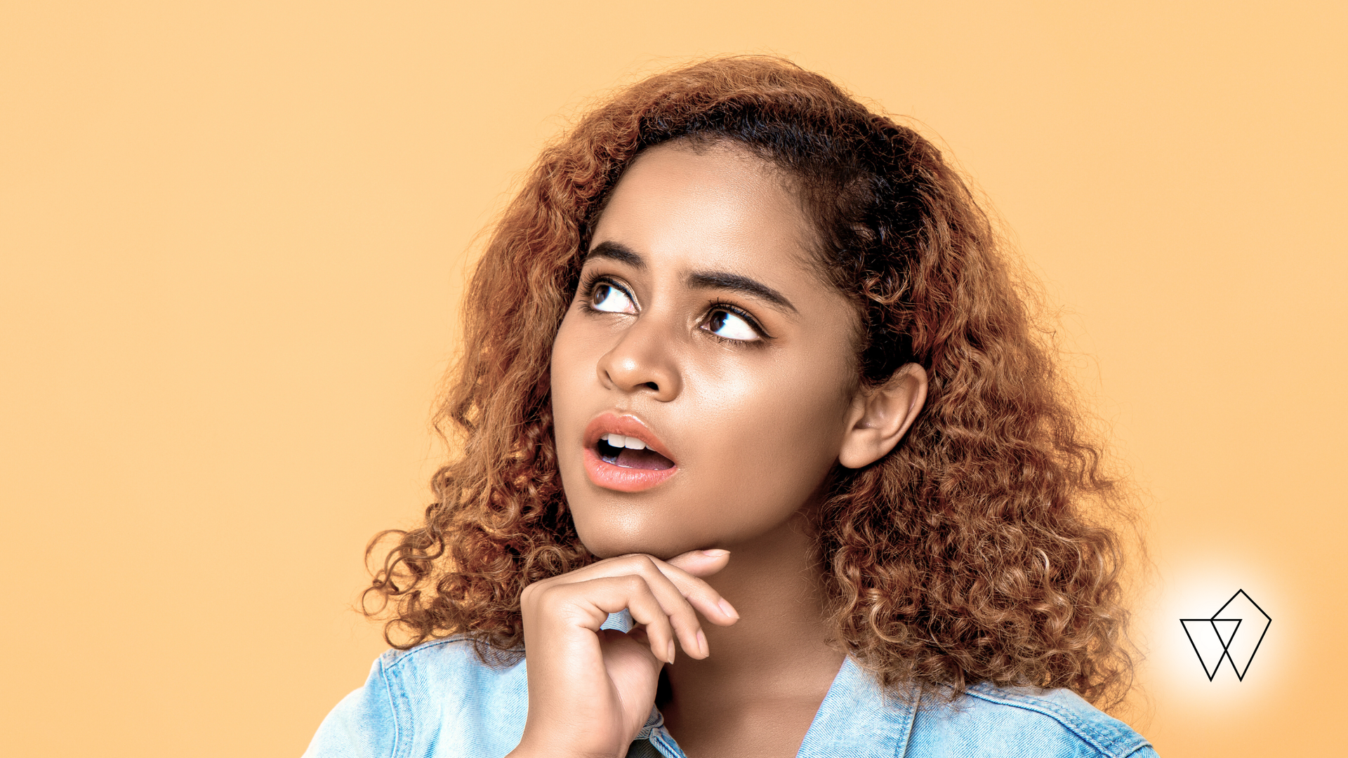 Woman with curly hair looking up thoughtfully, hand on chin, against a peach background.
