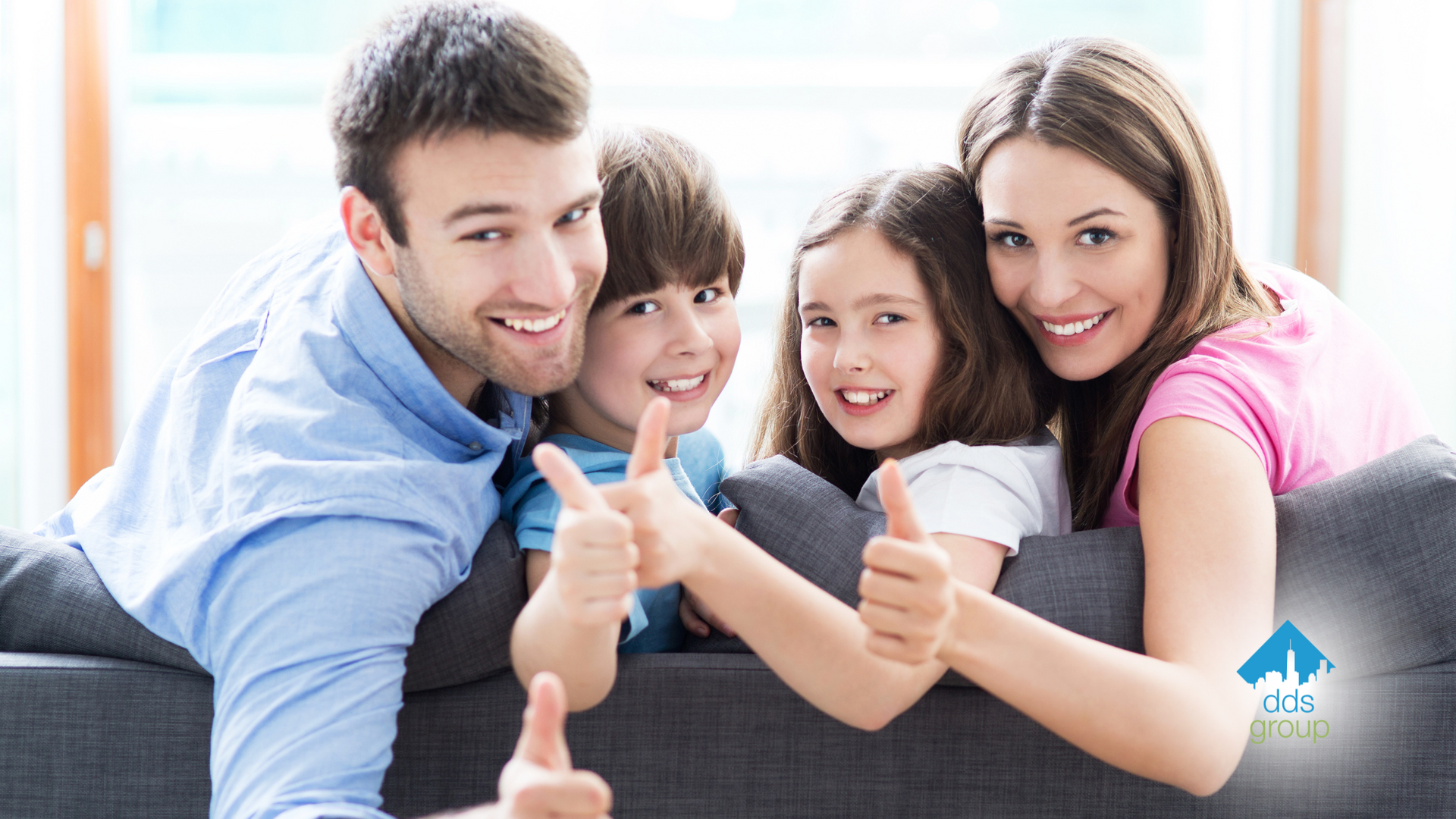 A family is sitting on a couch giving a thumbs up.