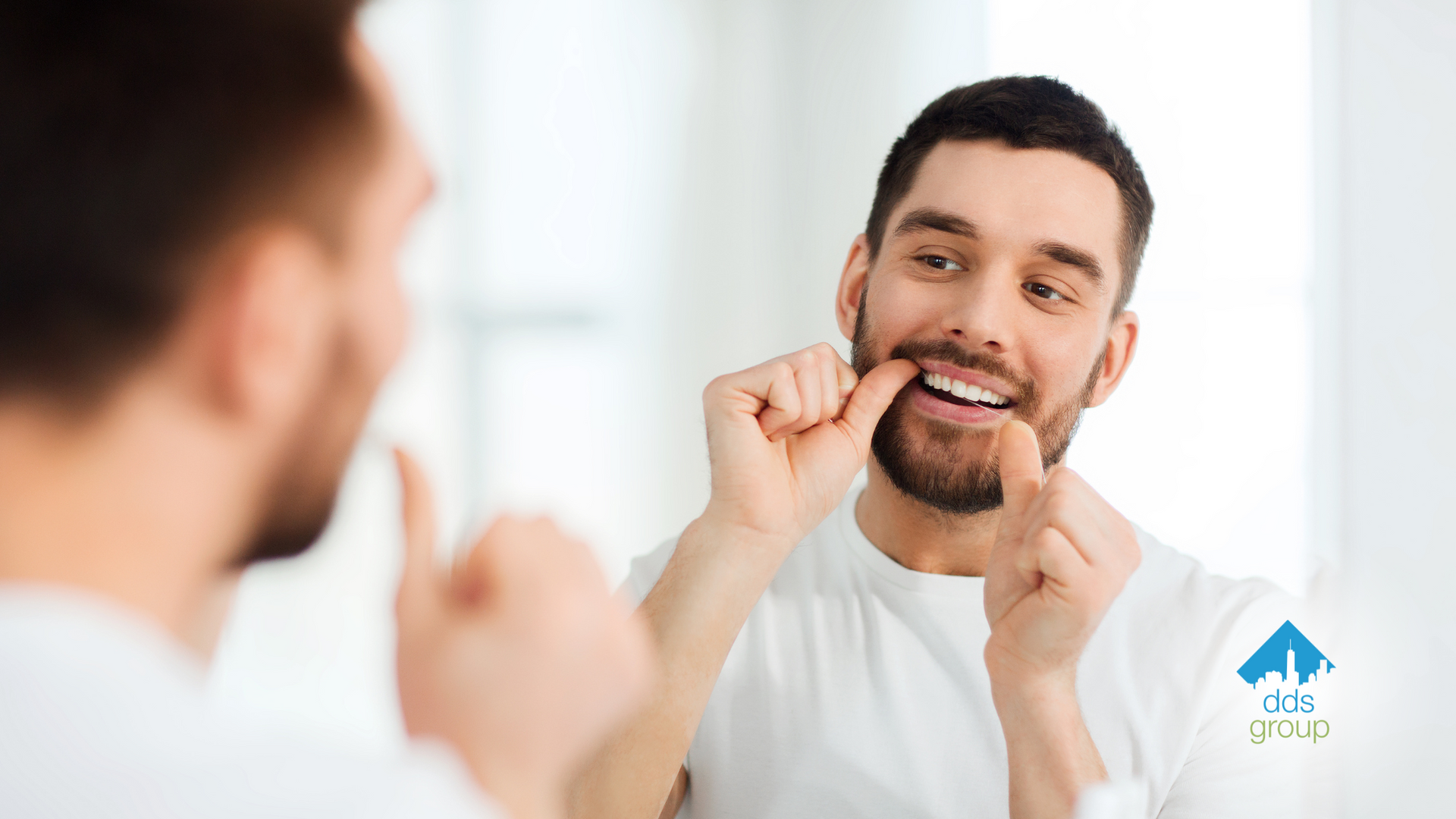 A man is flossing his teeth in front of a mirror.