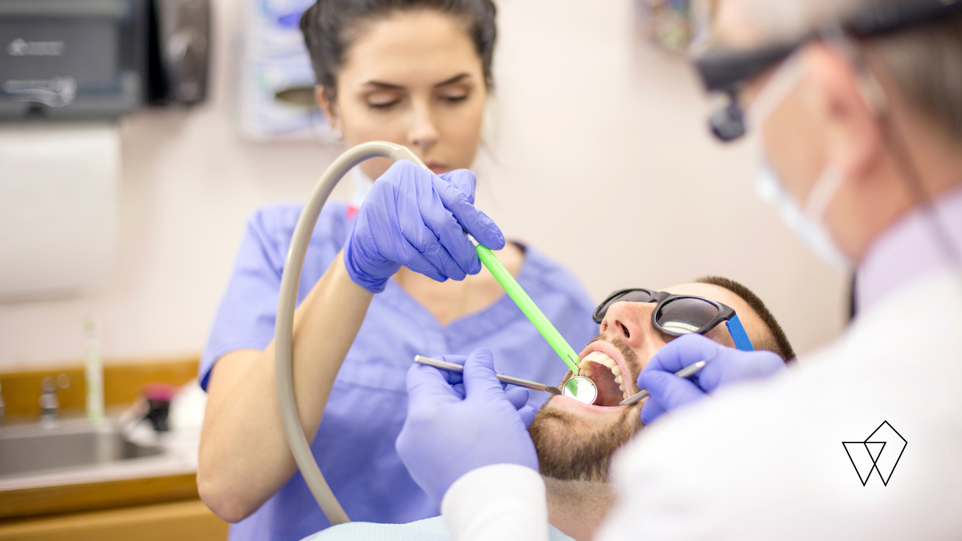 Dentist examining patient's teeth with dental assistant holding suction tube.