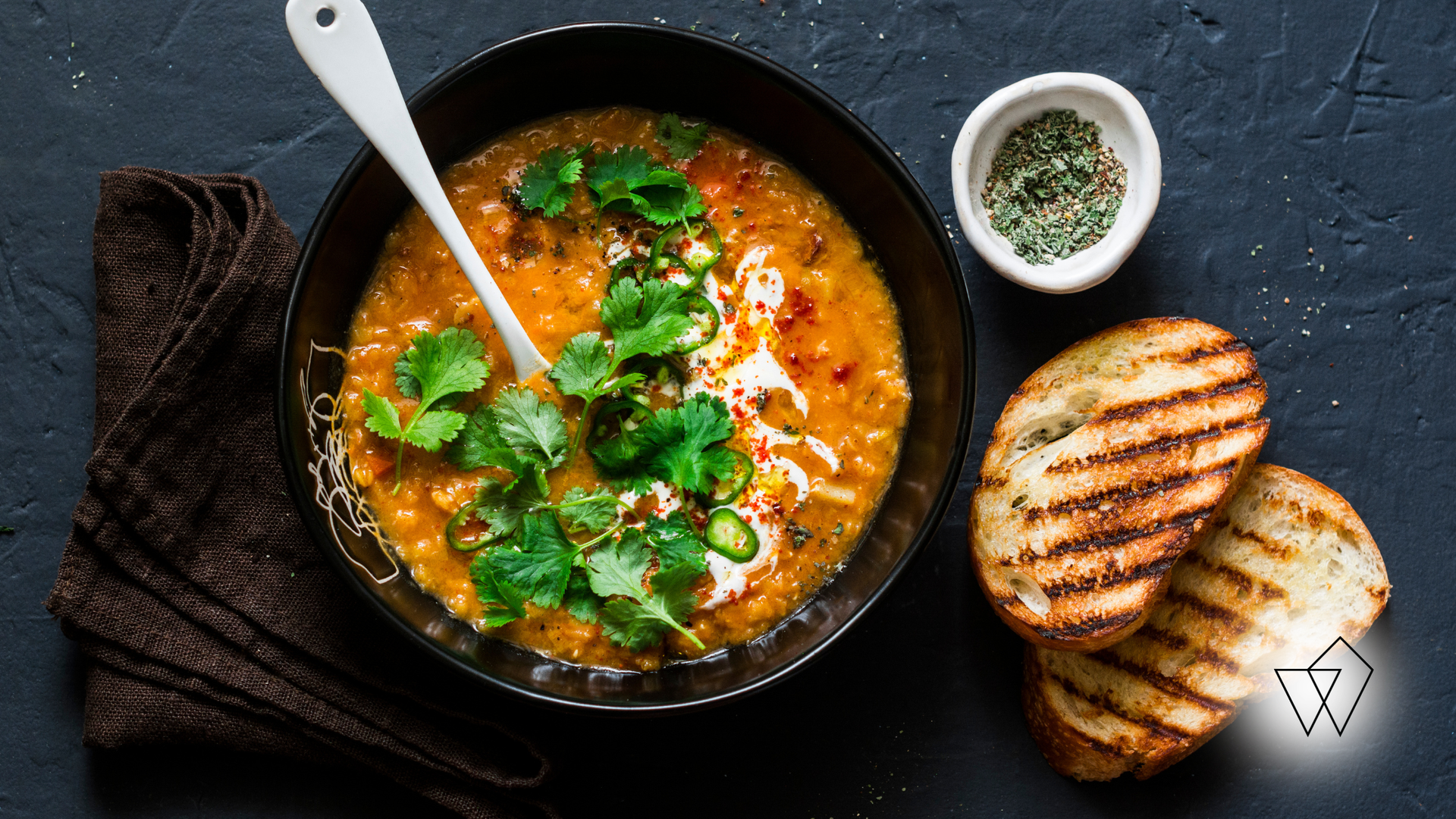 Bowl of lentil soup with grilled bread and garnish.
