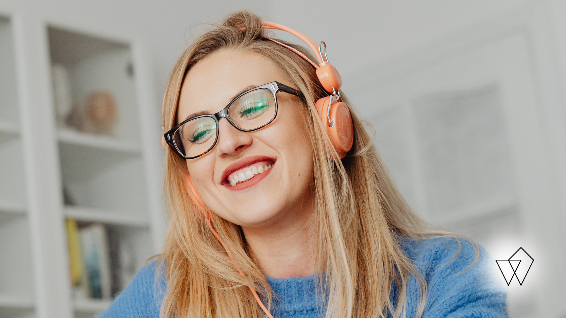 Smiling woman in glasses and headphones, wearing a blue sweater in a bright room