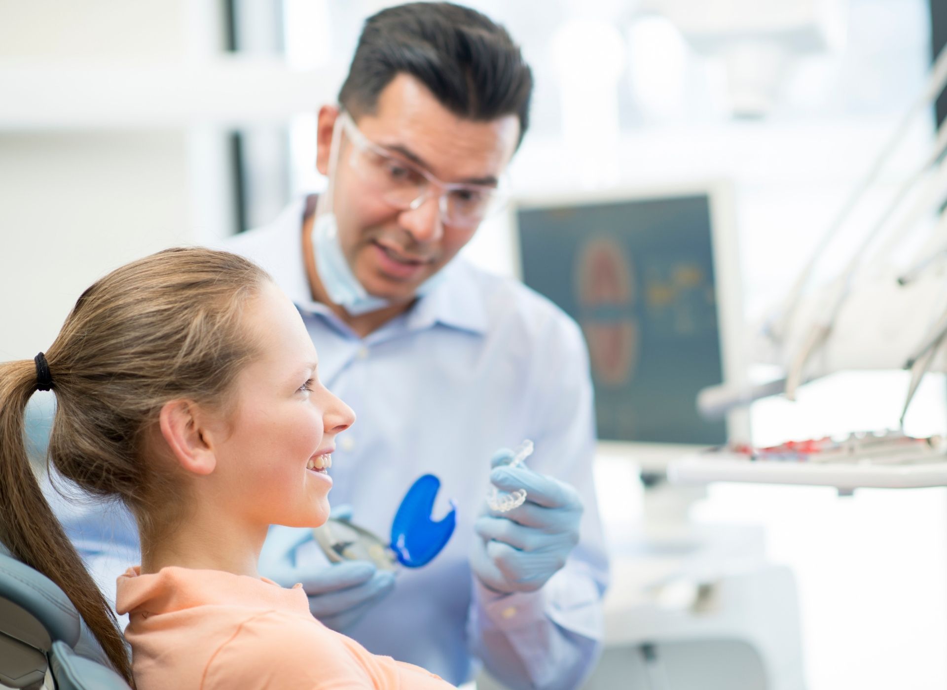 Dentist comparing tooth shade with a patient. Doctor's hands in pink gloves. Patient smiles. Clinic setting.