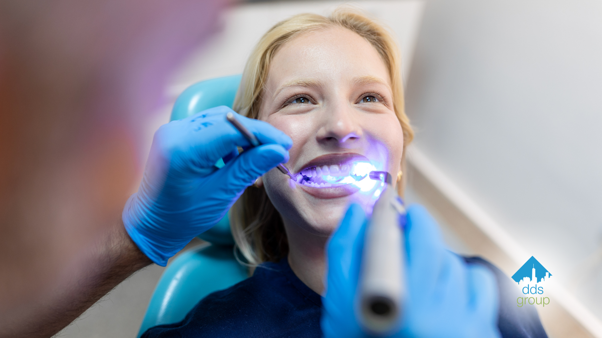 A woman is sitting in a dental chair getting her teeth whitened by a dentist.