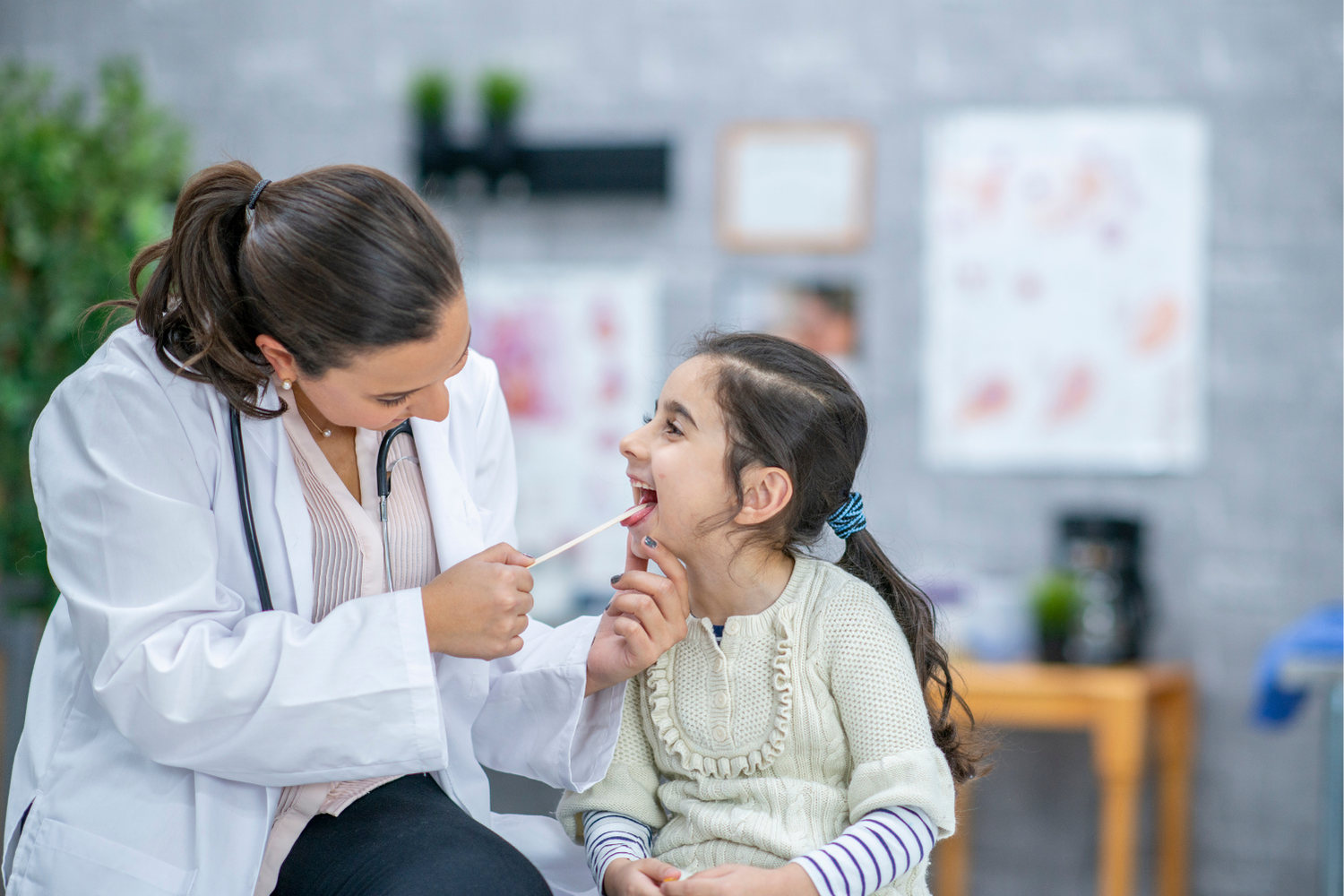 Doctor examining a child's throat with a tongue depressor in a medical office setting.