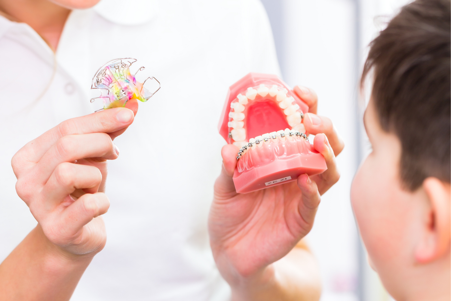 Dentist showing braces model to patient, holding a retainer.