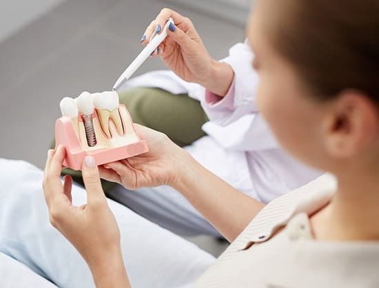 Dentist showing a dental implant model to a patient in an office setting.