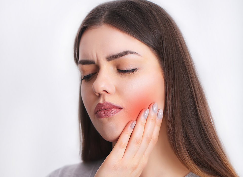 Woman with closed eyes, touching her cheek. Redness indicates pain, likely from dental issue.