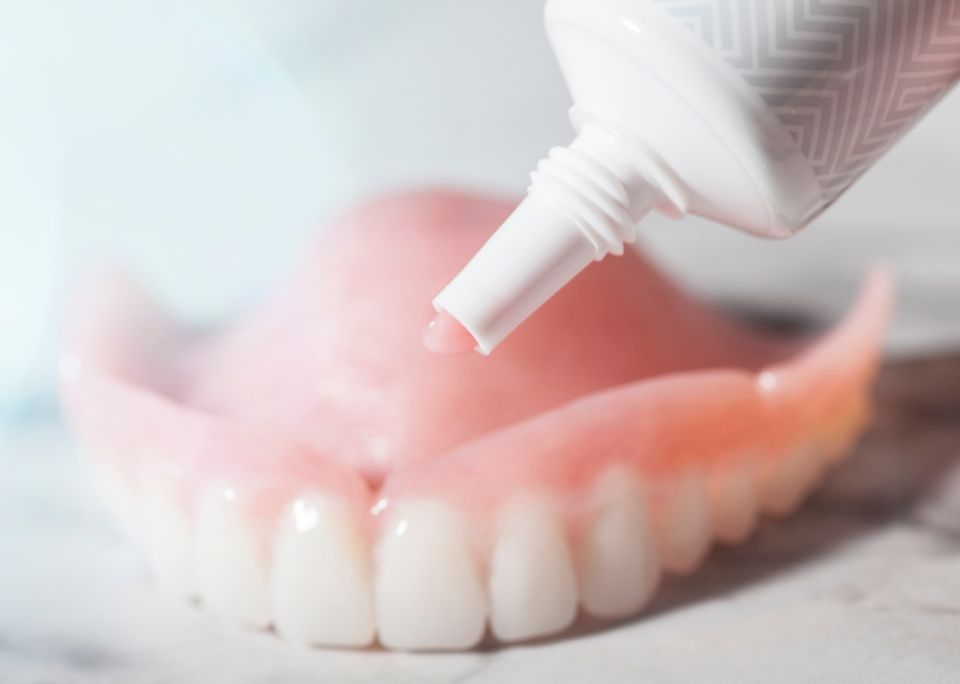Dentures with adhesive being applied from a tube; close-up shot.
