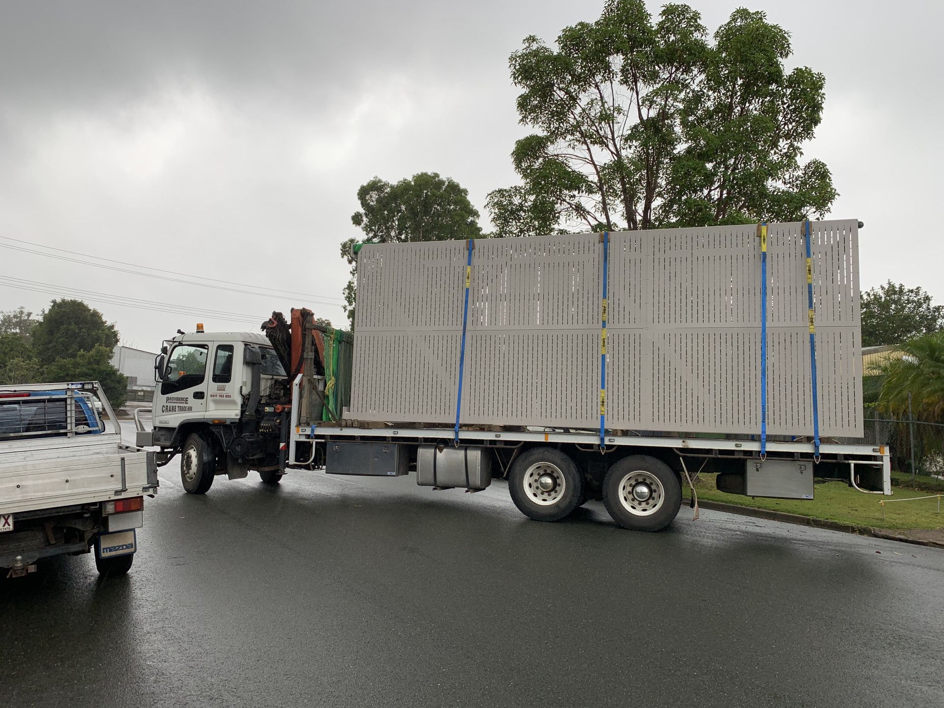 A white truck with a crane on the back is driving down a street. — Keystone Engineering Sheet Metal Industries in Noosaville, QLD