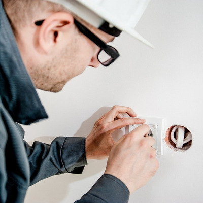 a man wearing a hard hat and glasses  working on an electrical outlet