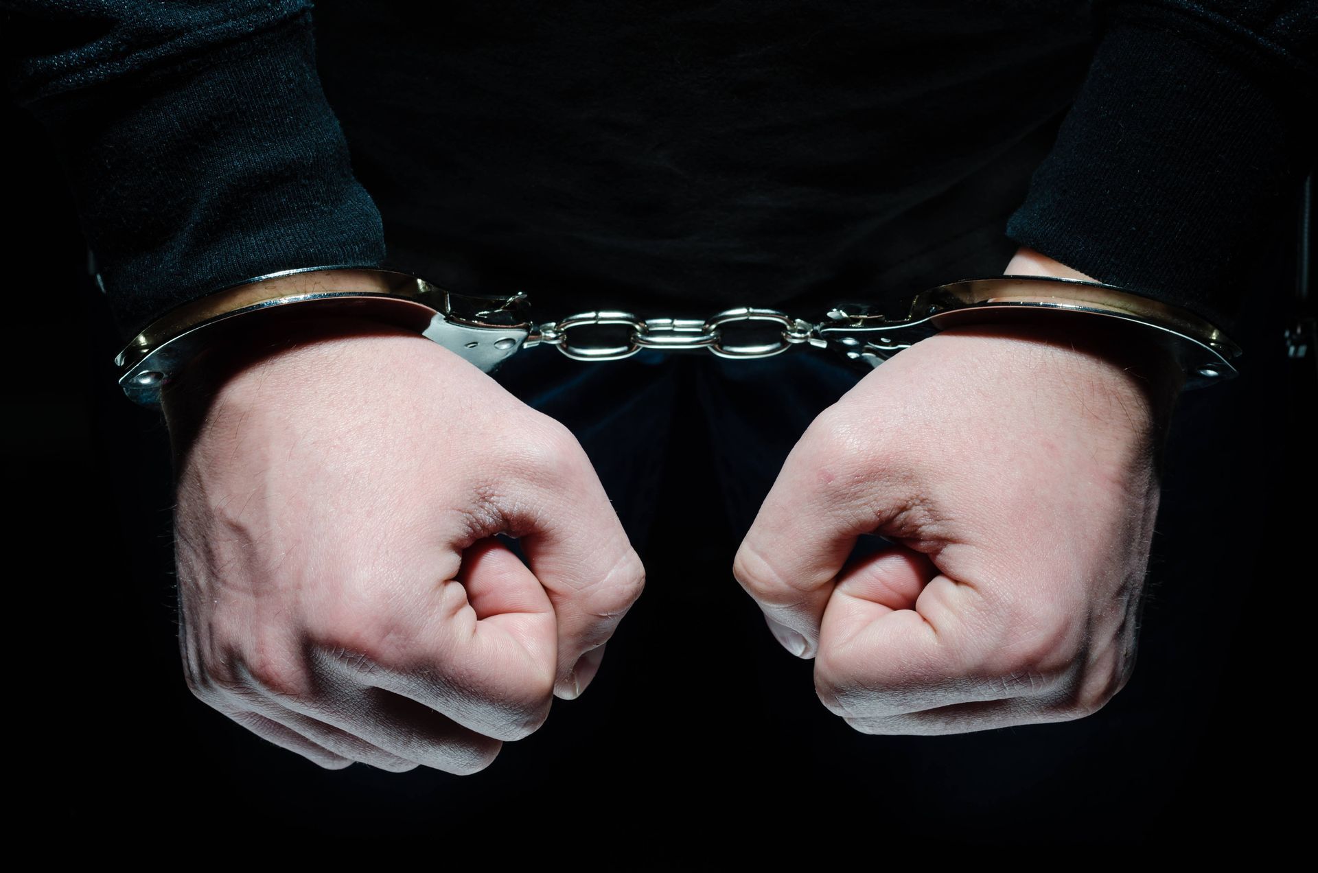 Hands in handcuffs, fists clenched, black background.