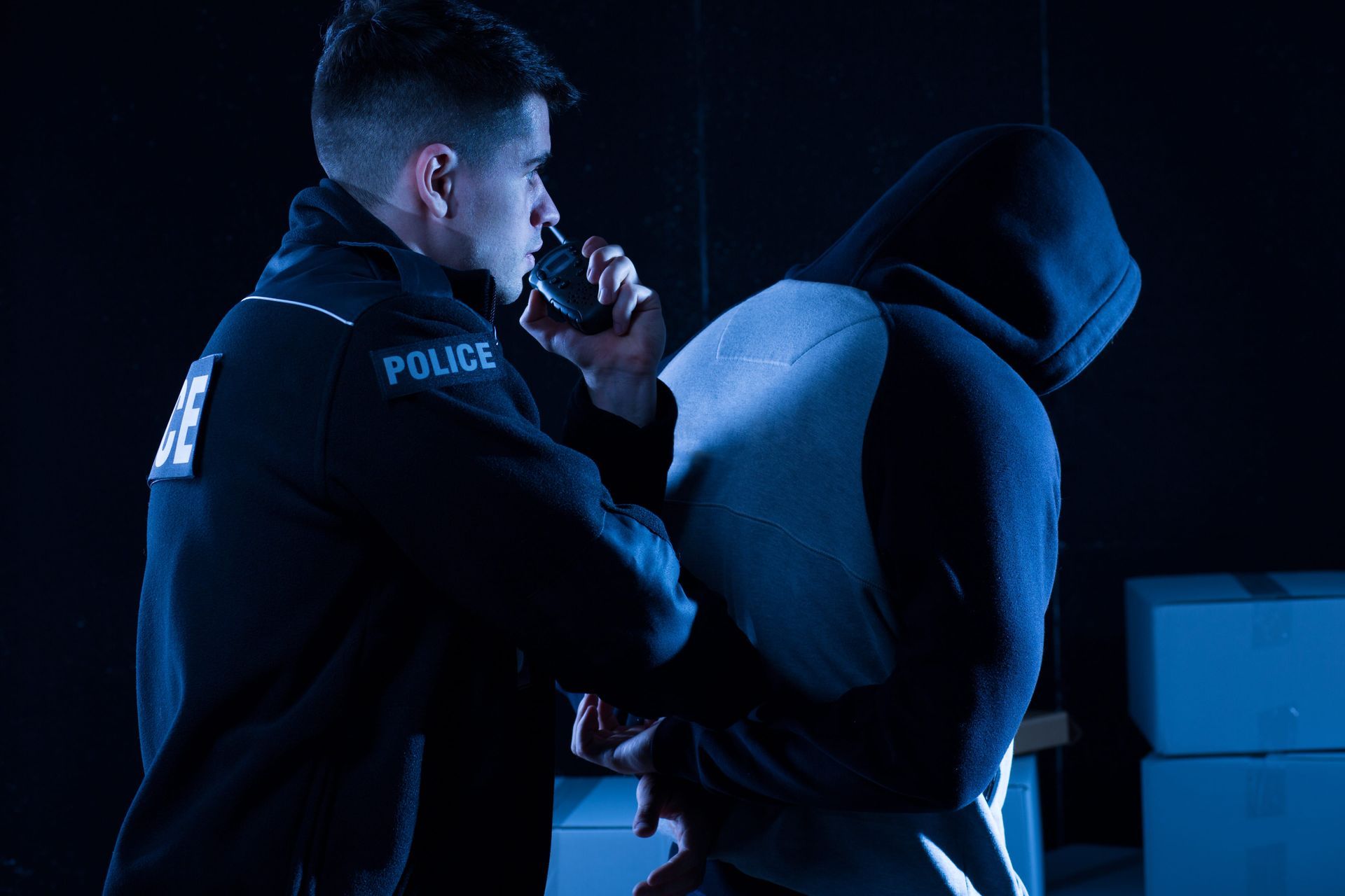 Police officer detaining a hooded suspect in a blue-lit scene