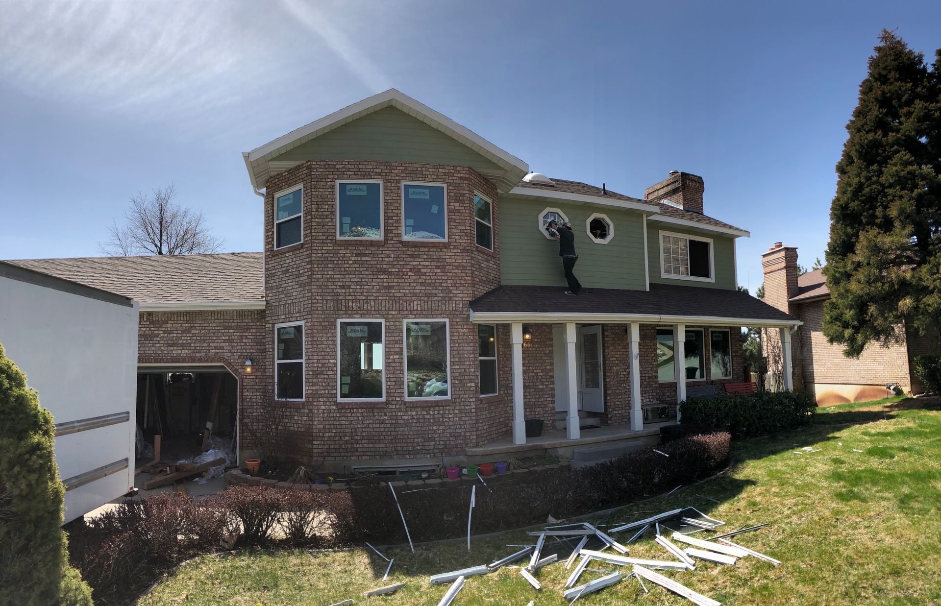 Two-story house with brick and green siding, porch, and yard on a sunny day.