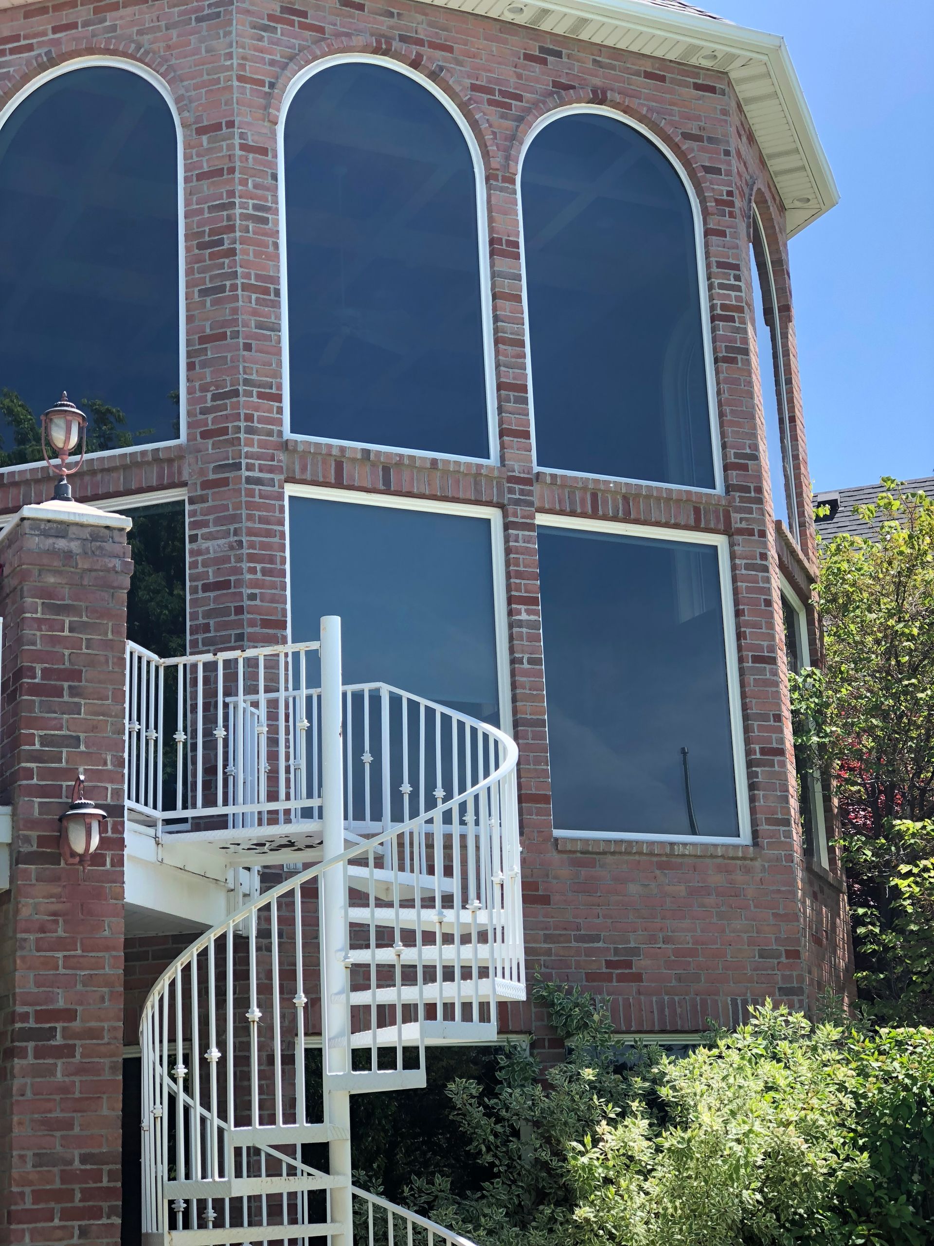 Brick house with large arched windows; white spiral staircase outside.