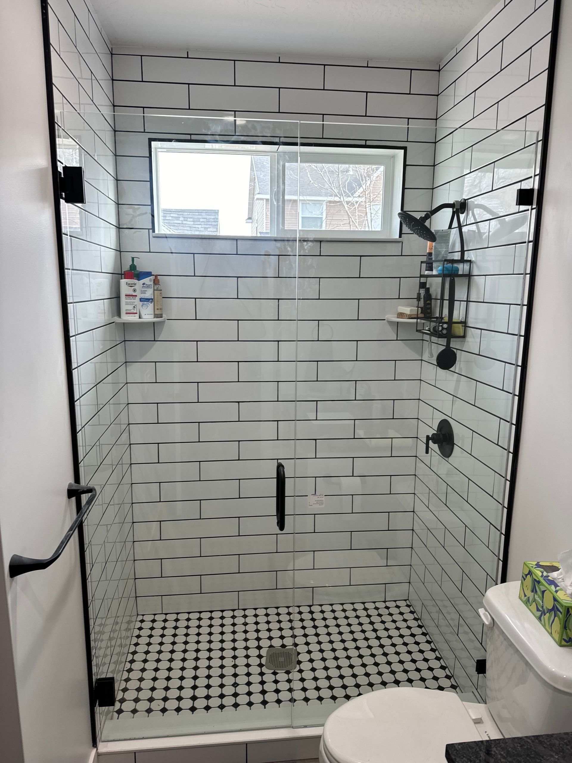 Small shower with white subway tile, black accents, and glass doors, located in a bathroom.