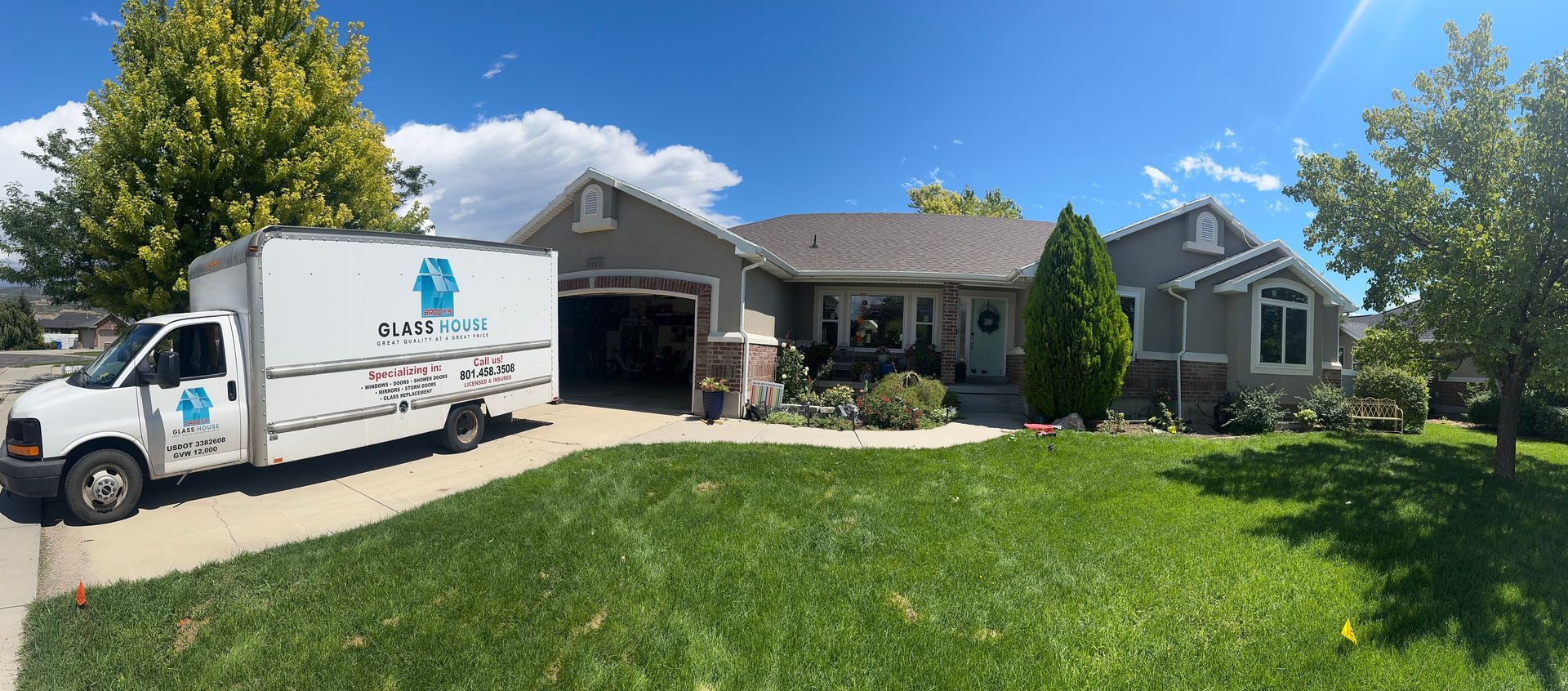 A moving truck parked in front of a gray house on a sunny day.