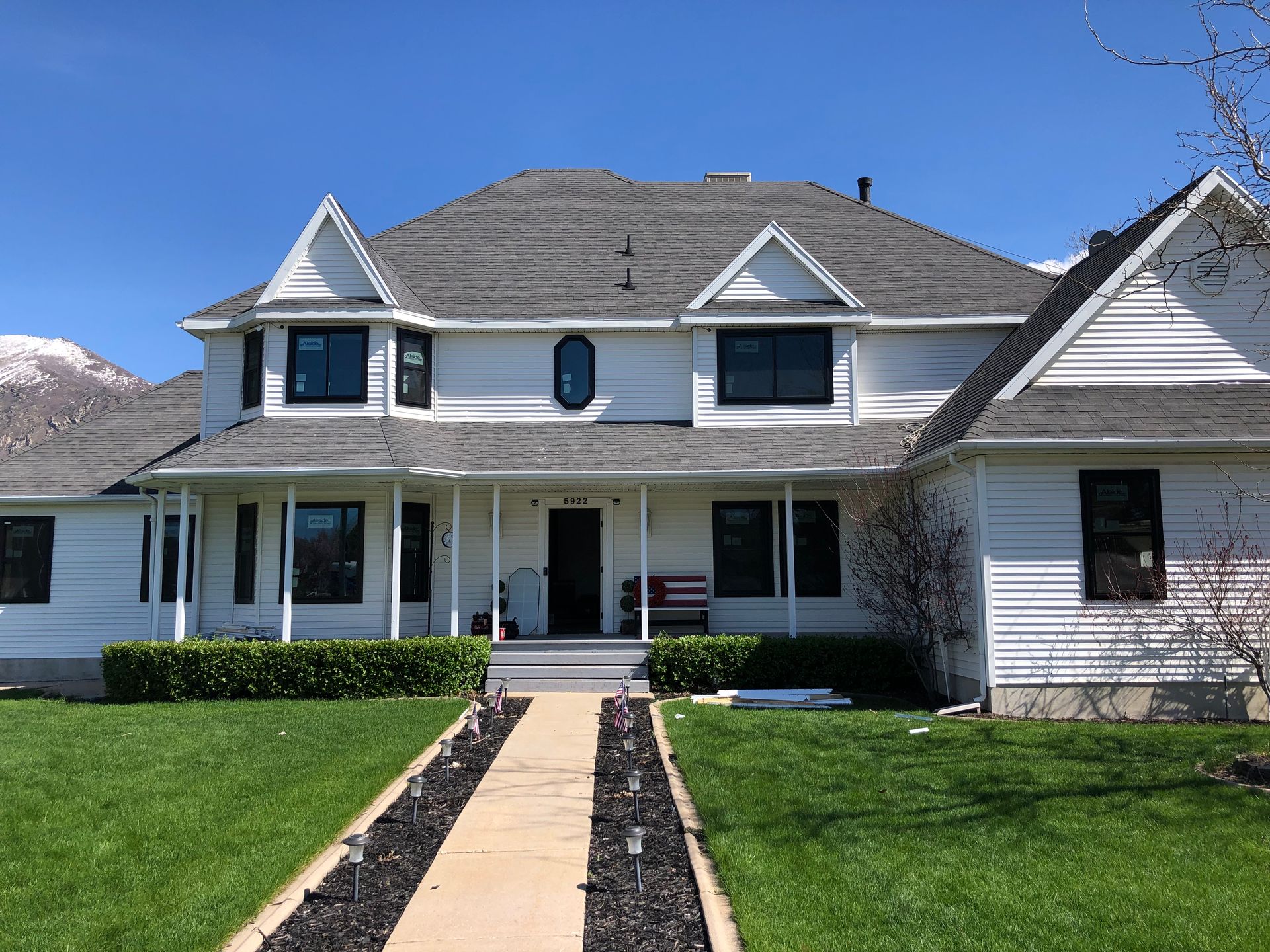 White two-story house with a gray roof, black window frames, and a green lawn. Clear blue sky.