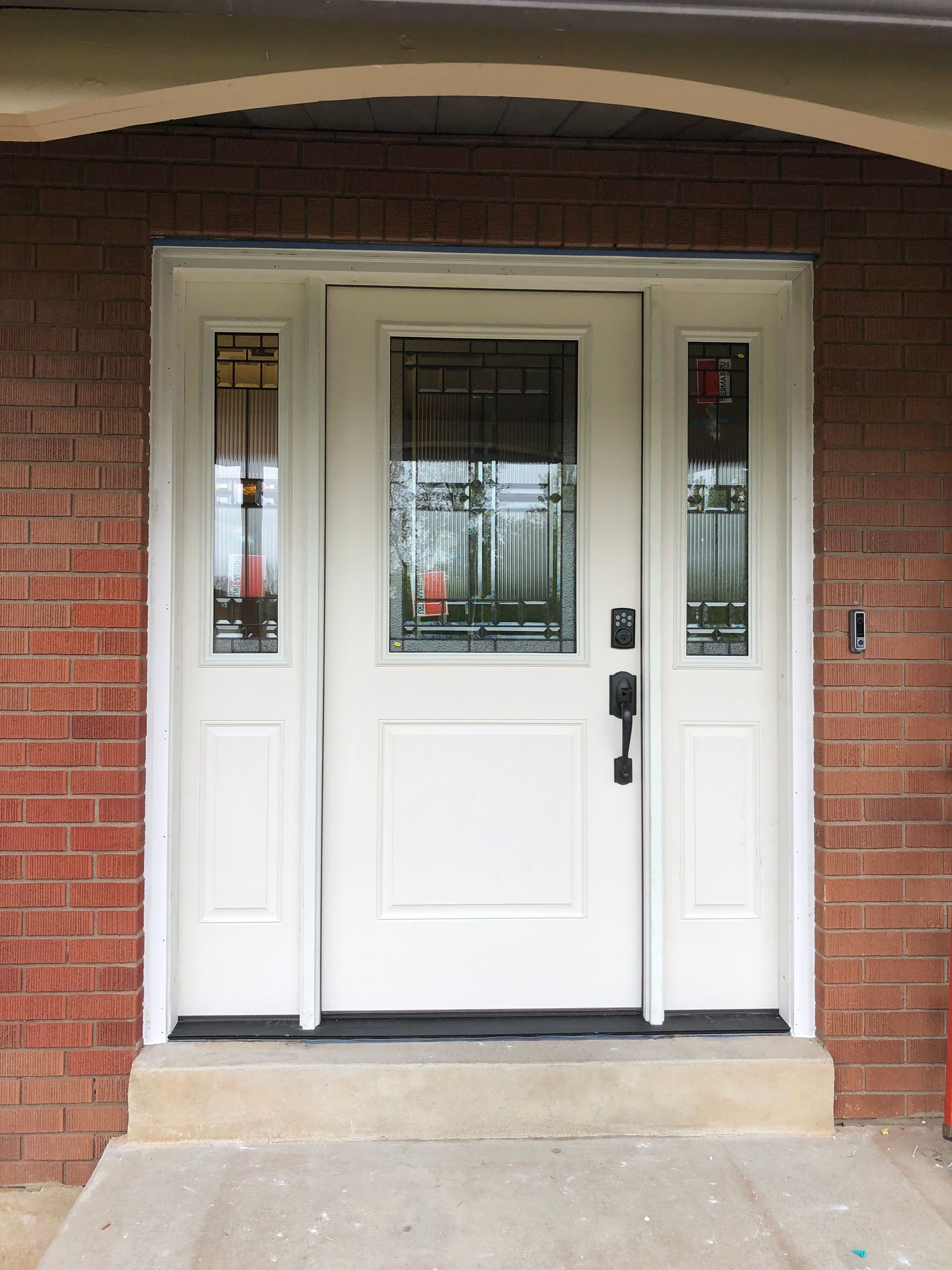 White front door with sidelights and a glass panel, set in a brick facade.