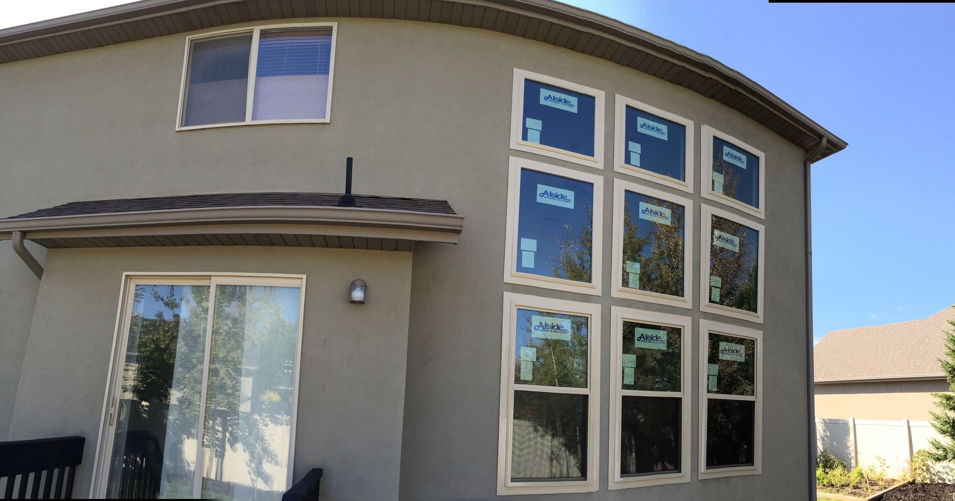 Exterior of a house with several newly installed windows; stucco siding, clear blue sky.