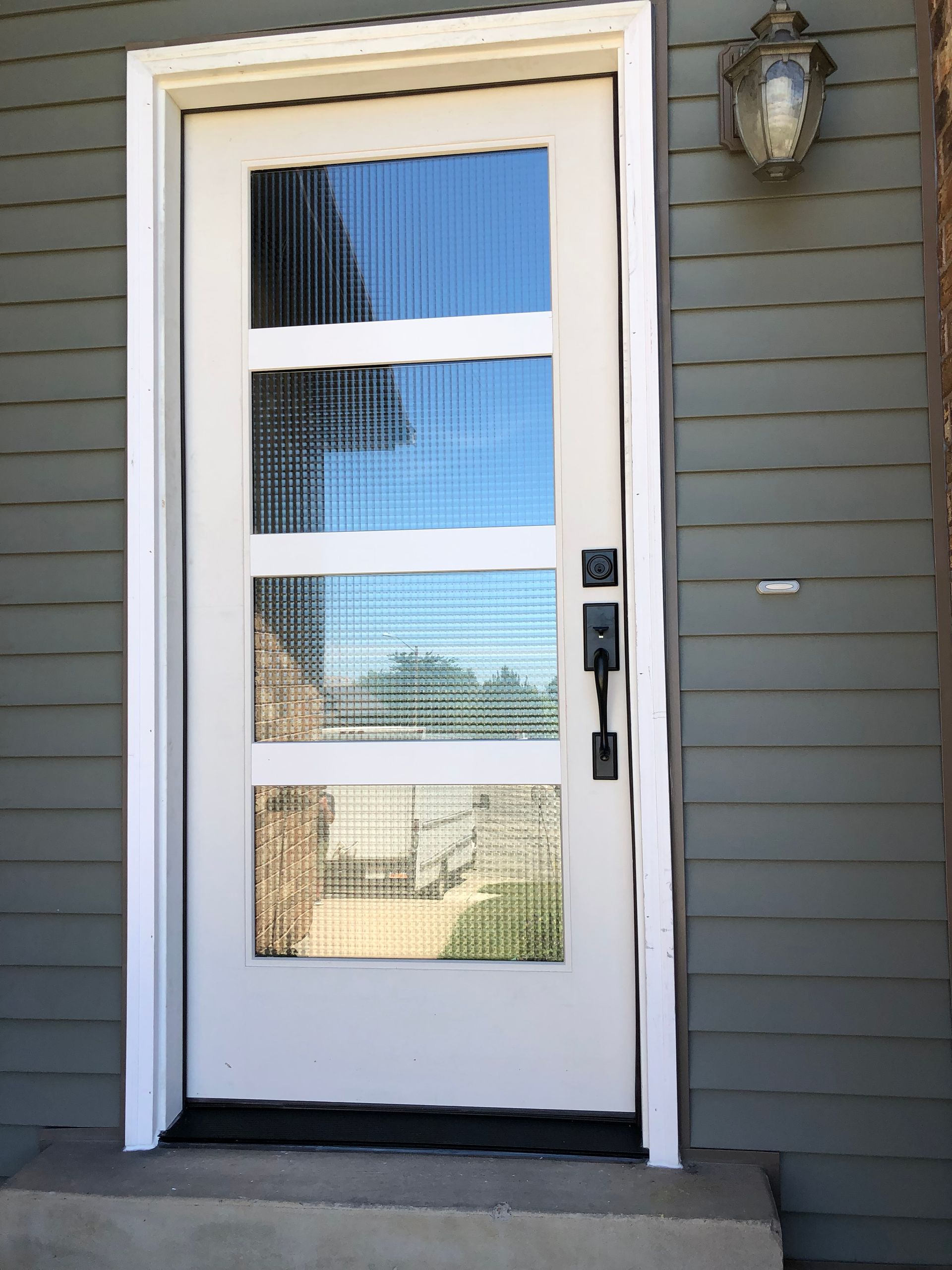White front door with four glass panels, black handle, set in a white frame.
