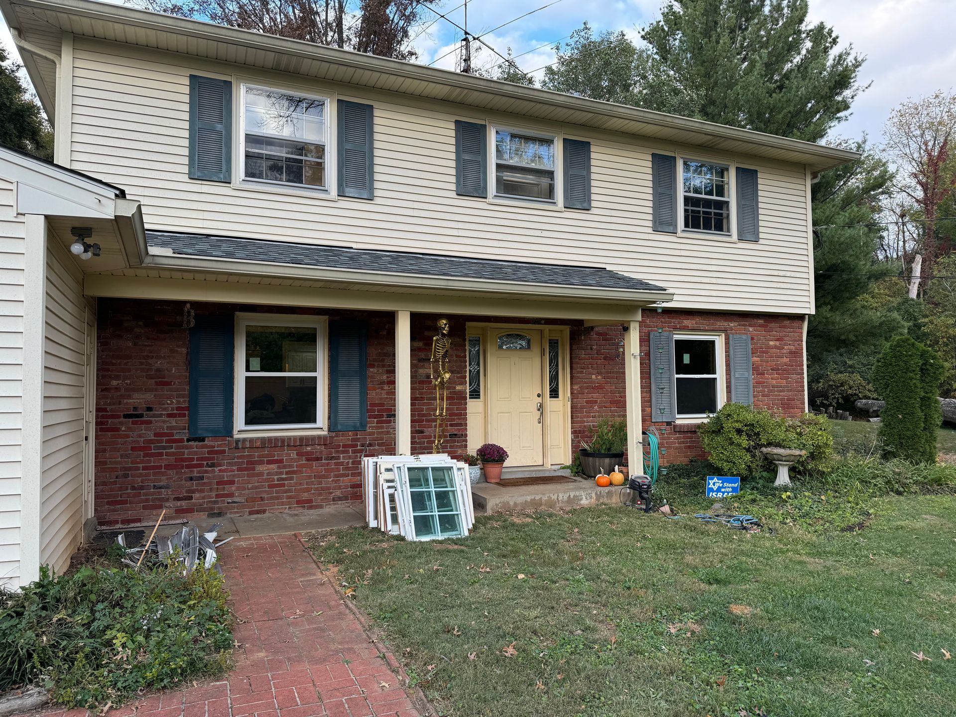 Two-story house with beige siding, brick facade, green shutters, and a lawn.
