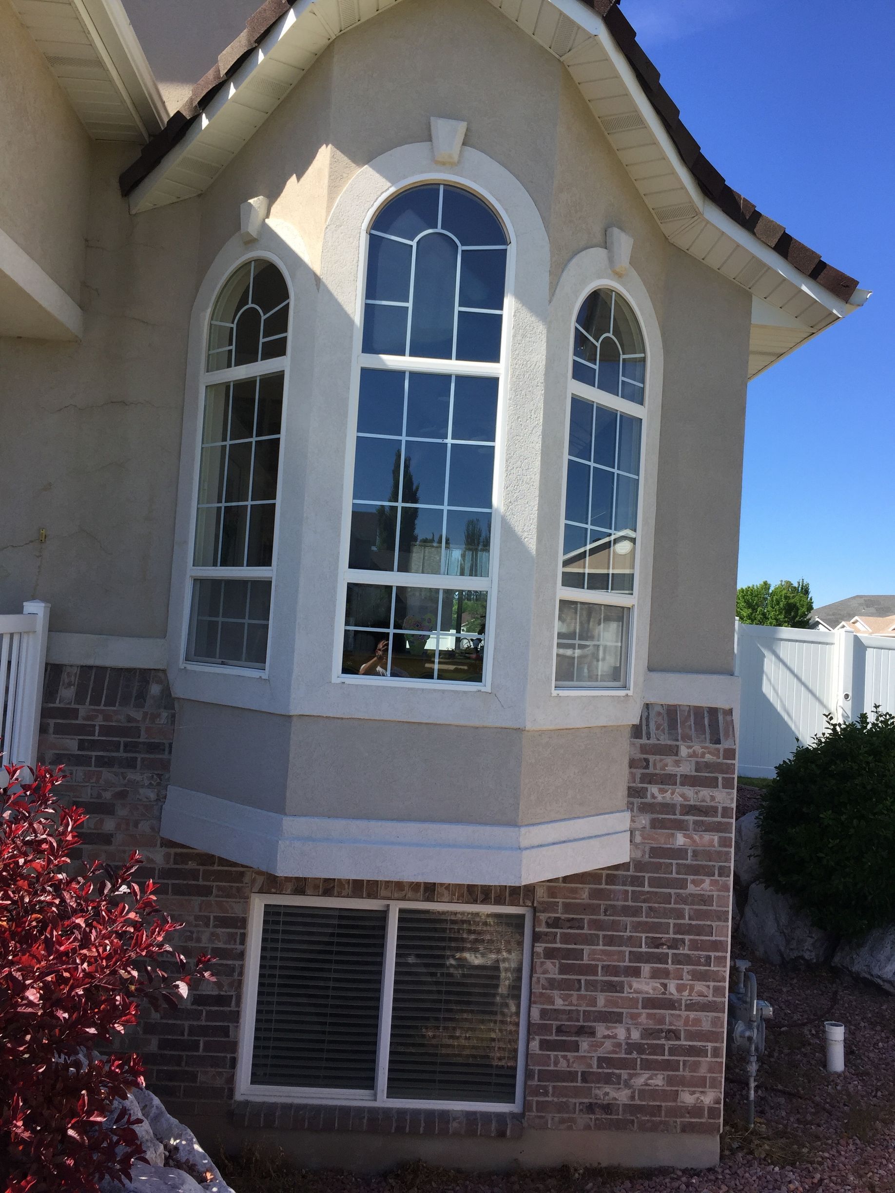 Bay window with arched top windows, over brick and tan exterior, on a house.