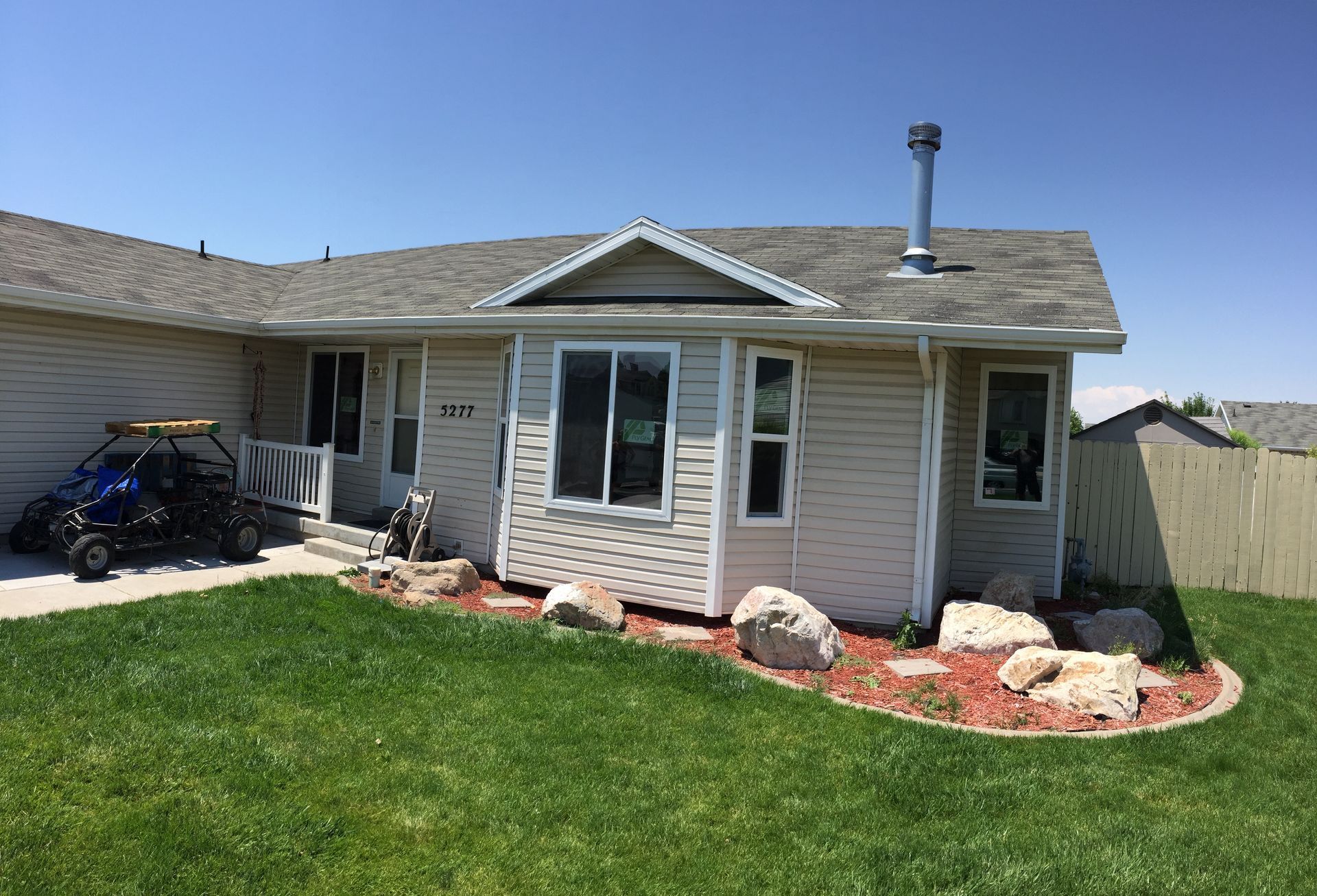 Beige house with green lawn and decorative rocks, blue sky in the background.