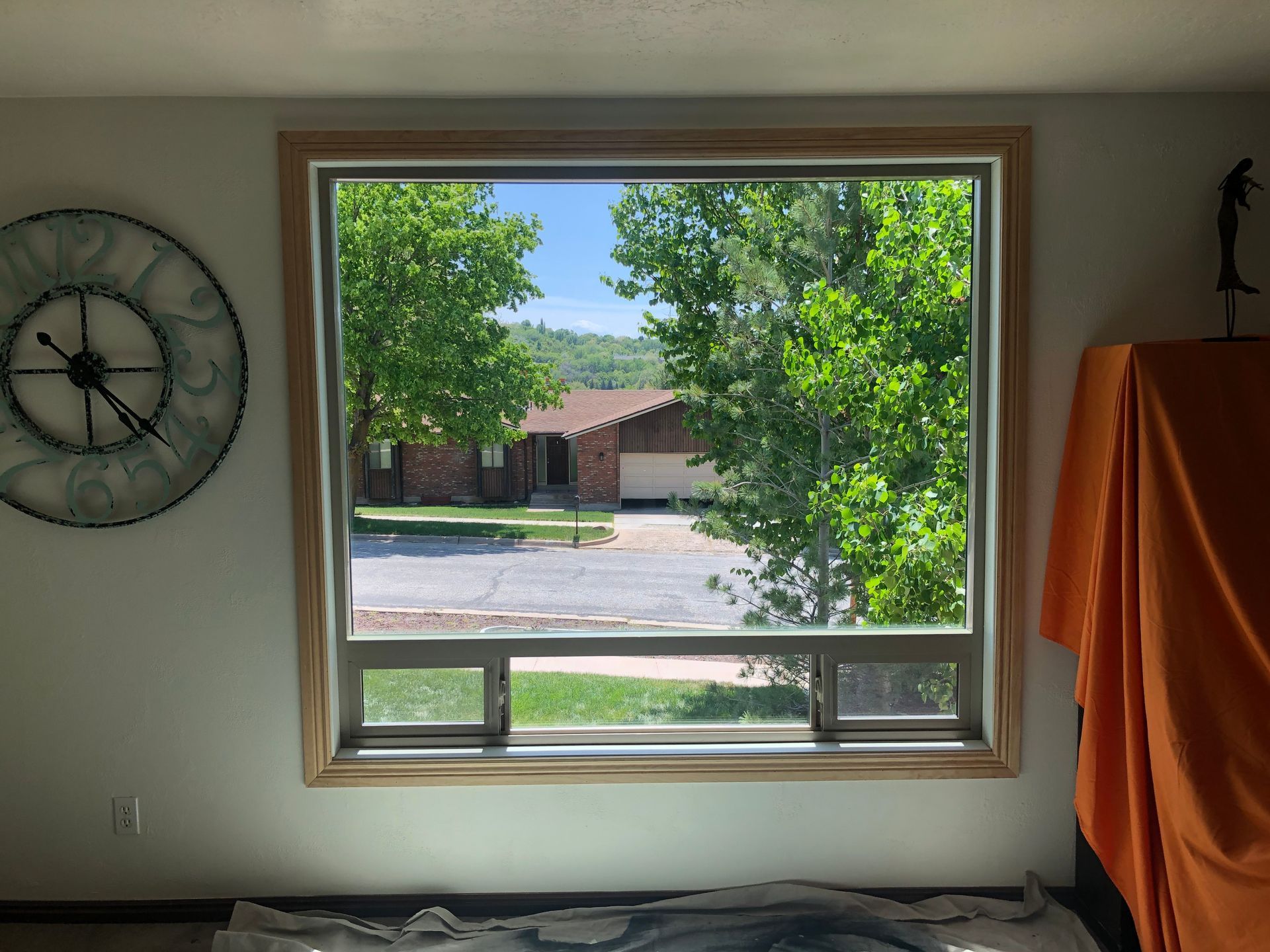 A window with a view of a street and trees; a clock and draped table are nearby.