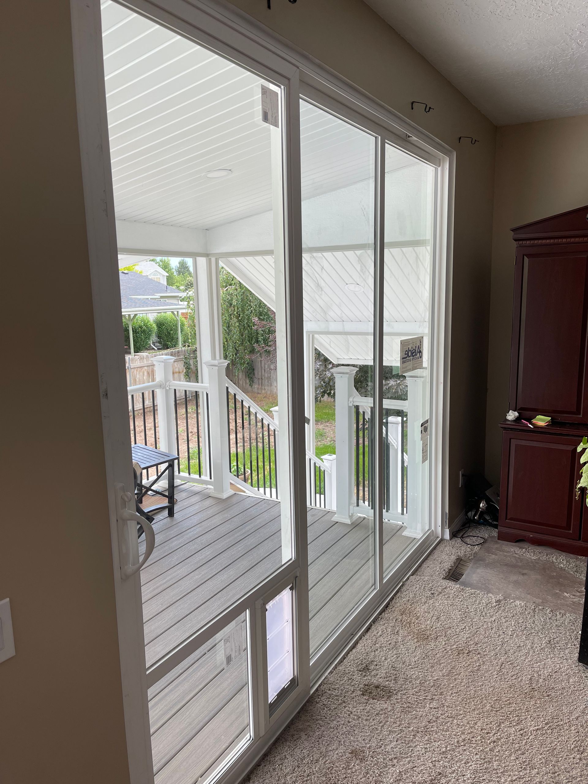 Sliding glass door with pet door leading to a deck, white frame, tan walls, brown cabinet.
