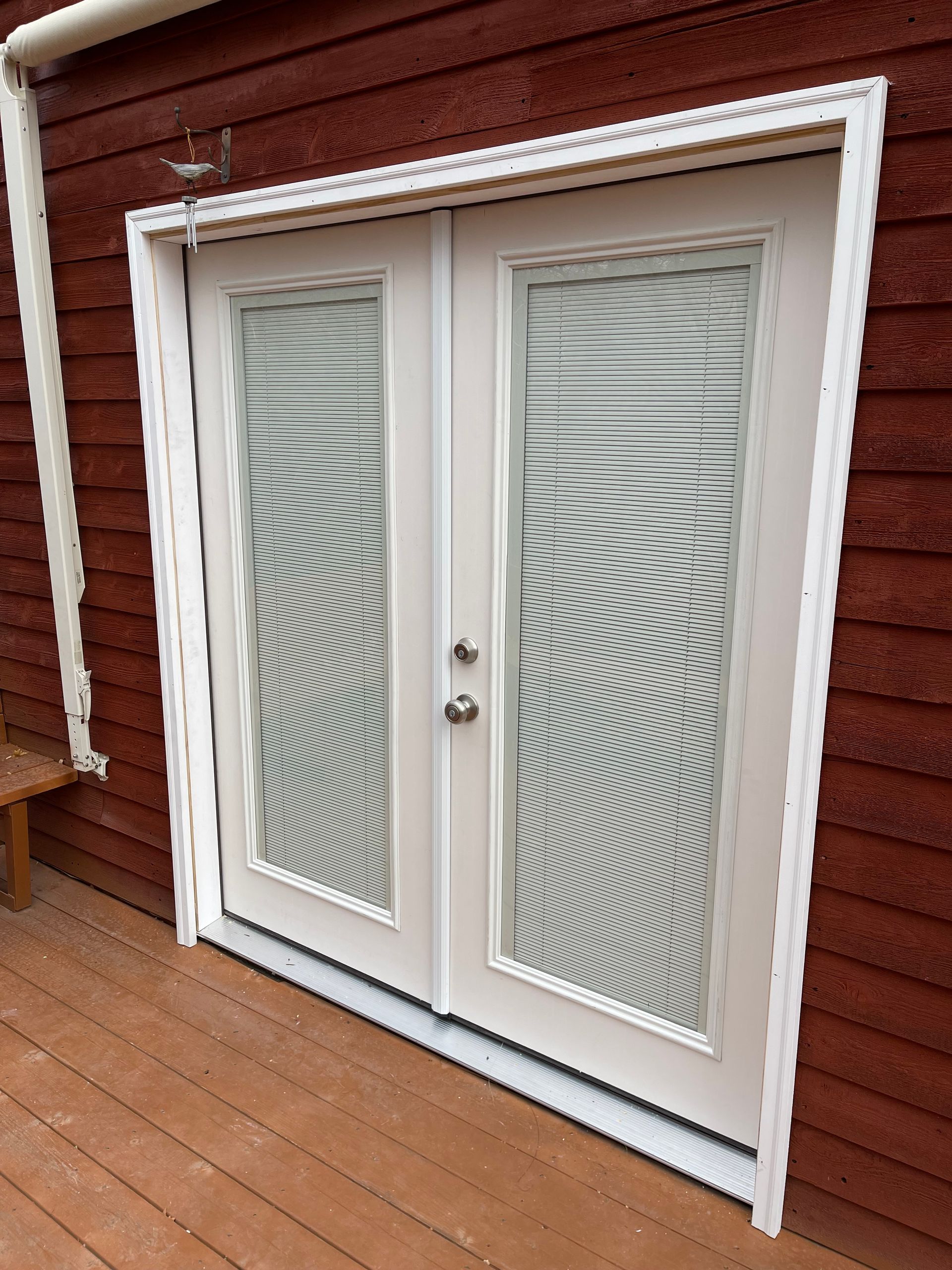 White double doors with decorative glass panels, set in a red exterior wall, on a wooden deck.