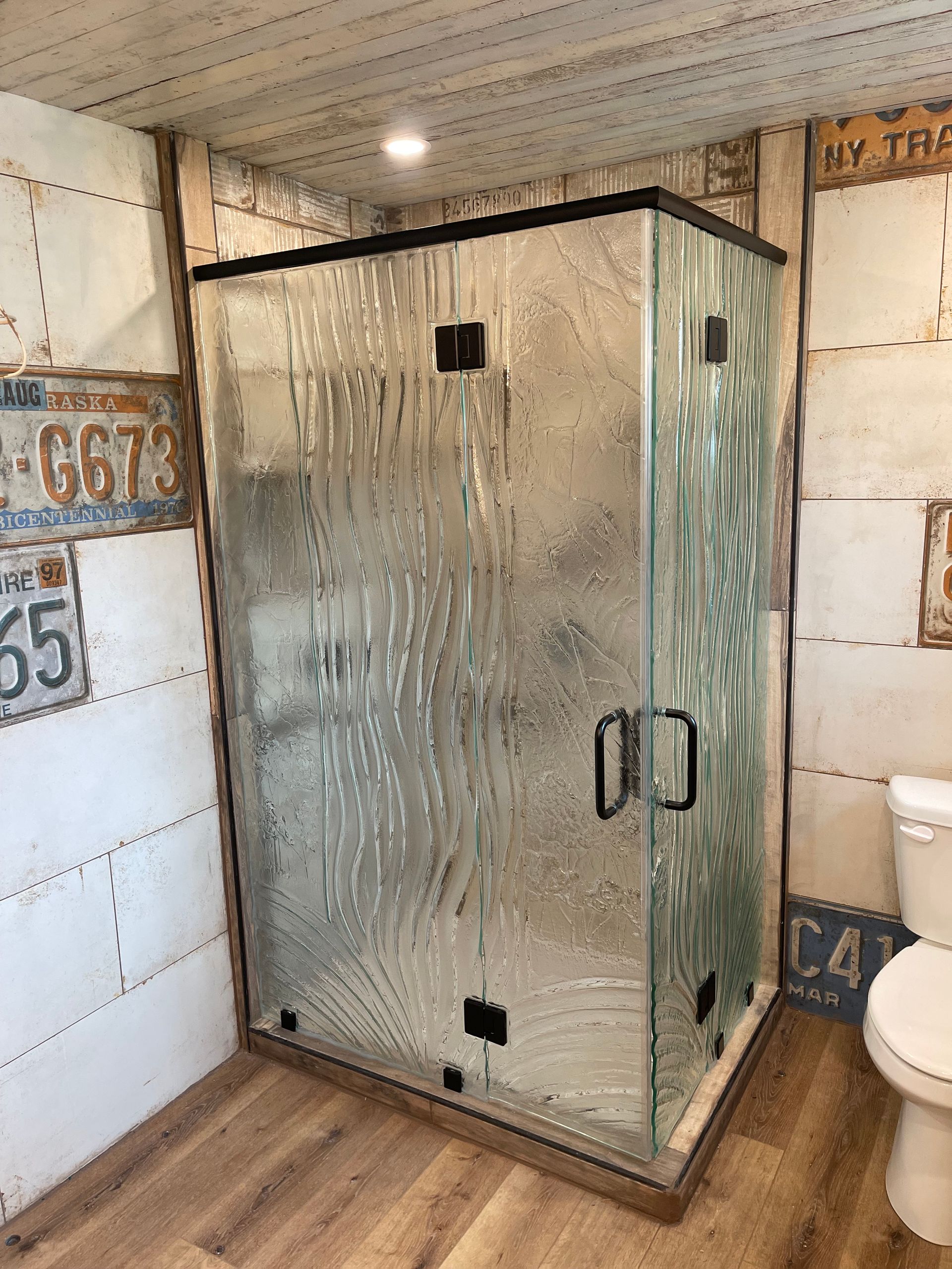 Glass shower with textured glass and black trim, in a bathroom with license plate-covered walls.